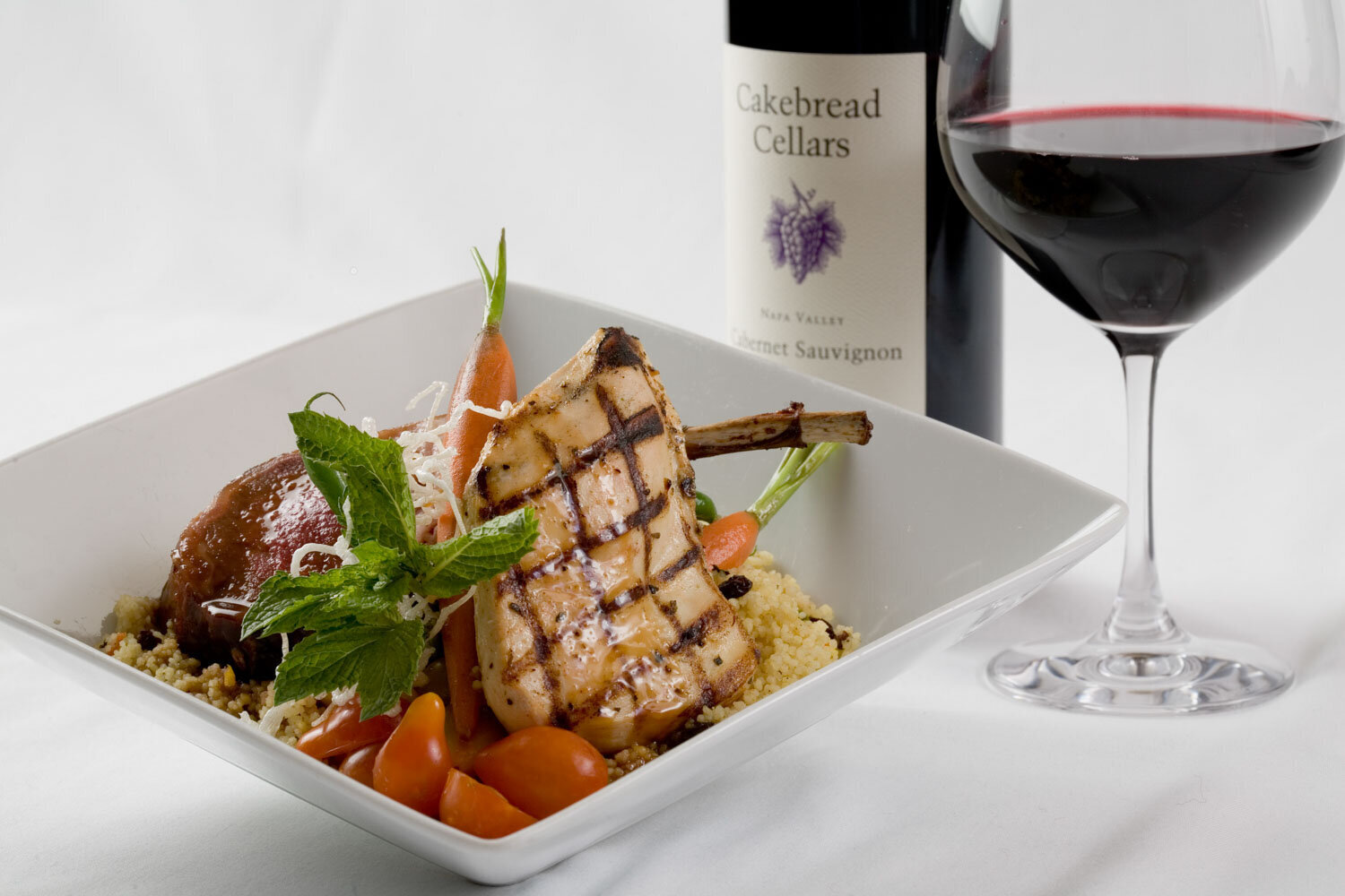 Grilled pork chop dish with wine bottle and glass of red wine
