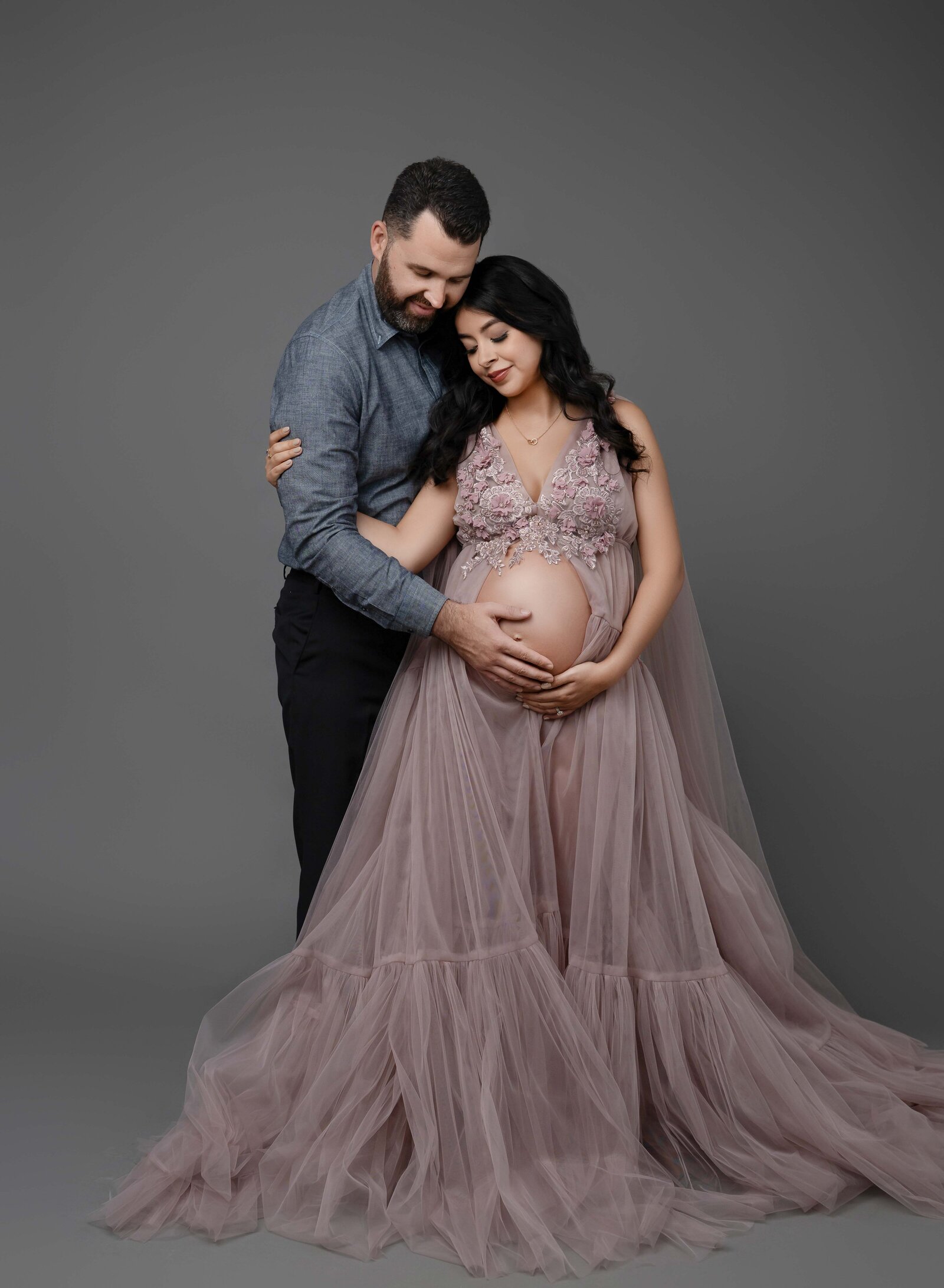 Mom holding onto Dad's arm and Dad holding baby bump and cuddling with Mom. Pregnancy photo taken by Jenni. Nikki Photography at Atlanta Photo Studio. 