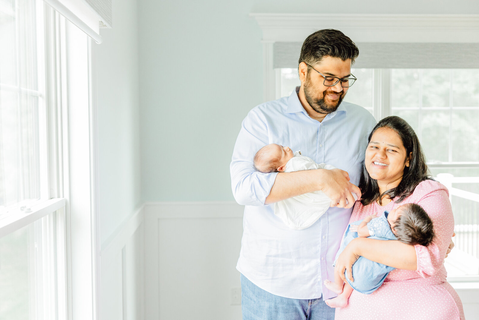 Dad smiles at his wife, who smiles toward the viewer, while each parent holds a baby