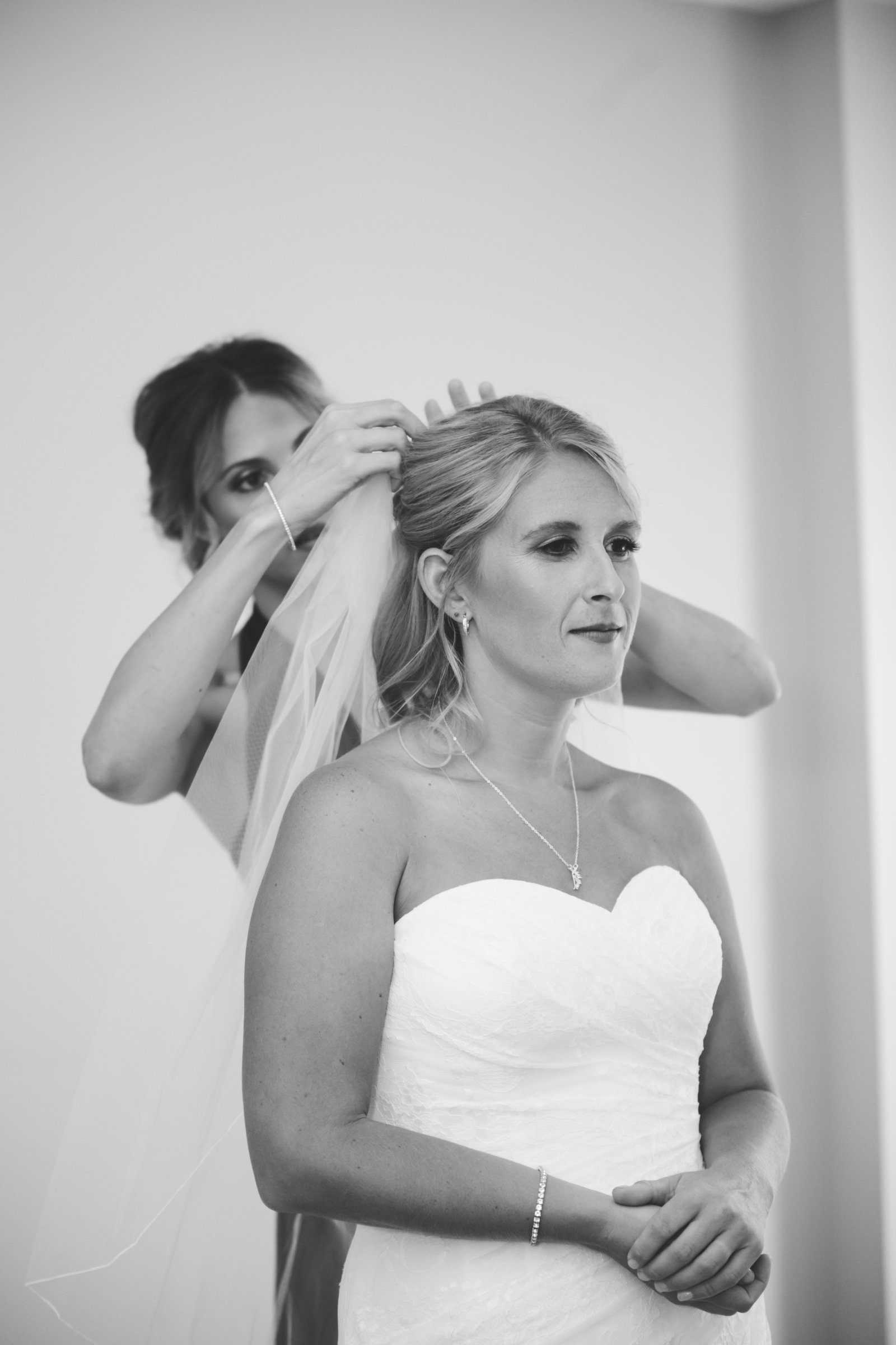bride stands as her bridesmaid adjusts her veil