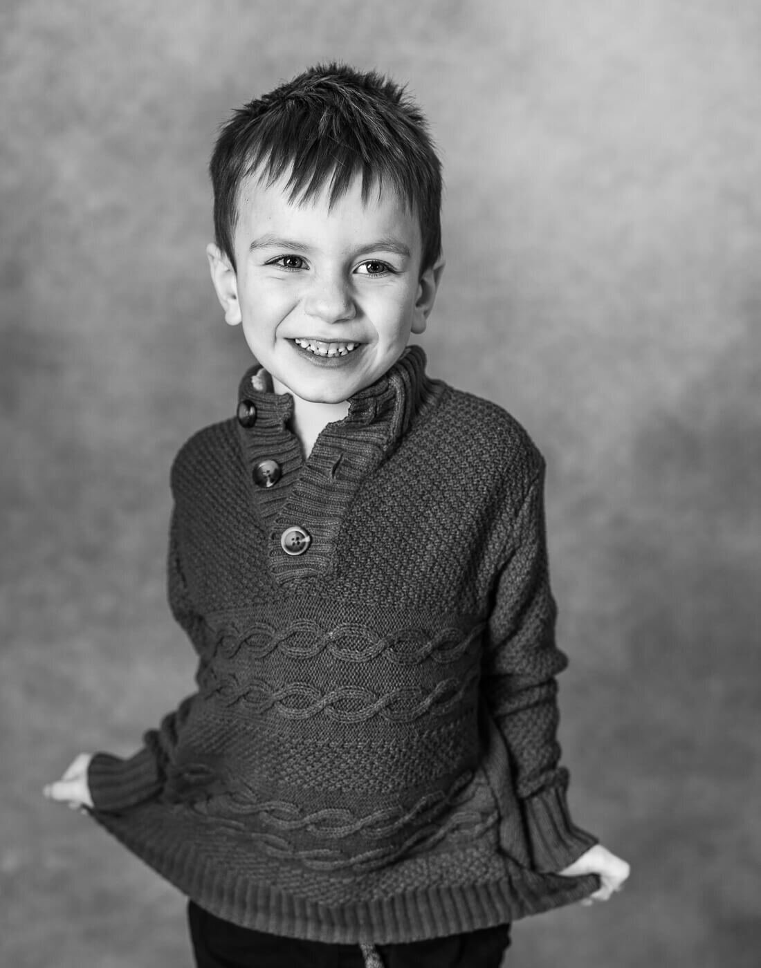 A kid smiles while holding their sweater.