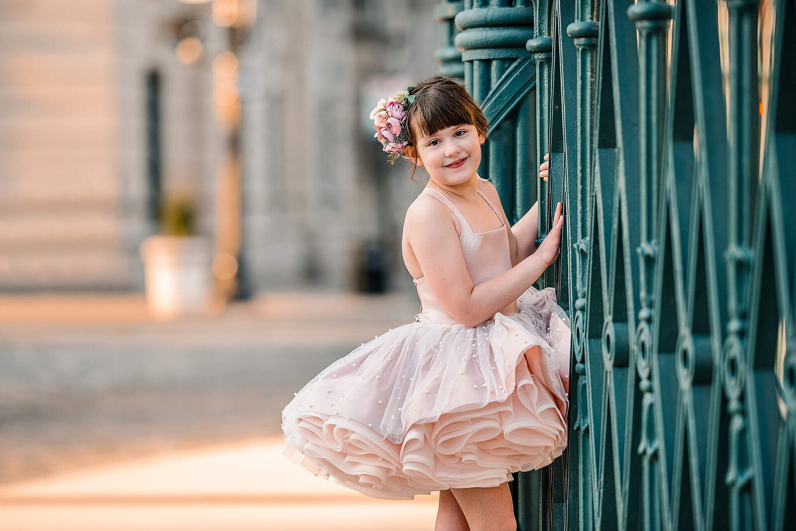 Girl in a pink dress with two hands on a green fence in Mount Vernon Baltimore Maryland