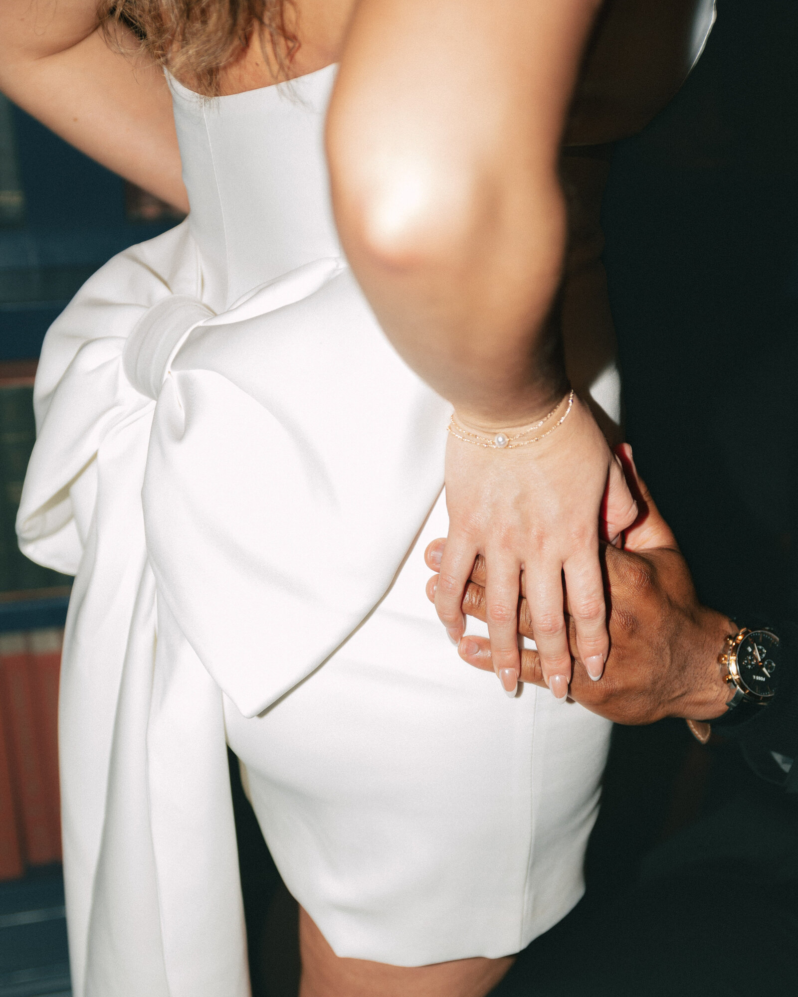 modern direct flash photograph of man holding womans hips. she wears a white satin dress with a large white bow on the back, austin engagement session