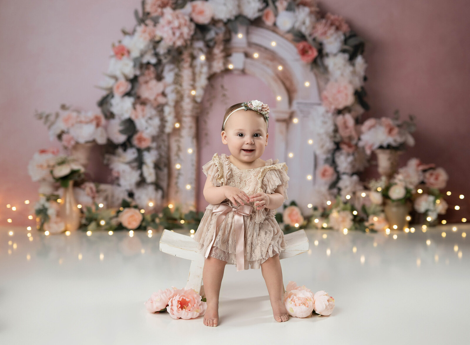 Baby girl sitting on stool in front of floral arch. Photographed at Atlanta Cake Smash photo studio.