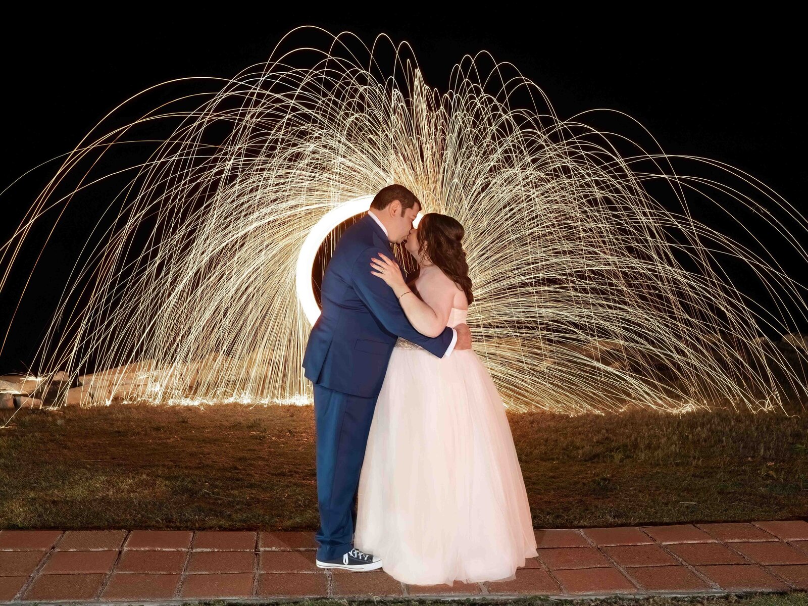 The bride and groom embrace under a stunning sparkler art display at night, captured during a Hatteras Island, NC wedding, showcasing magical and creative wedding photography.