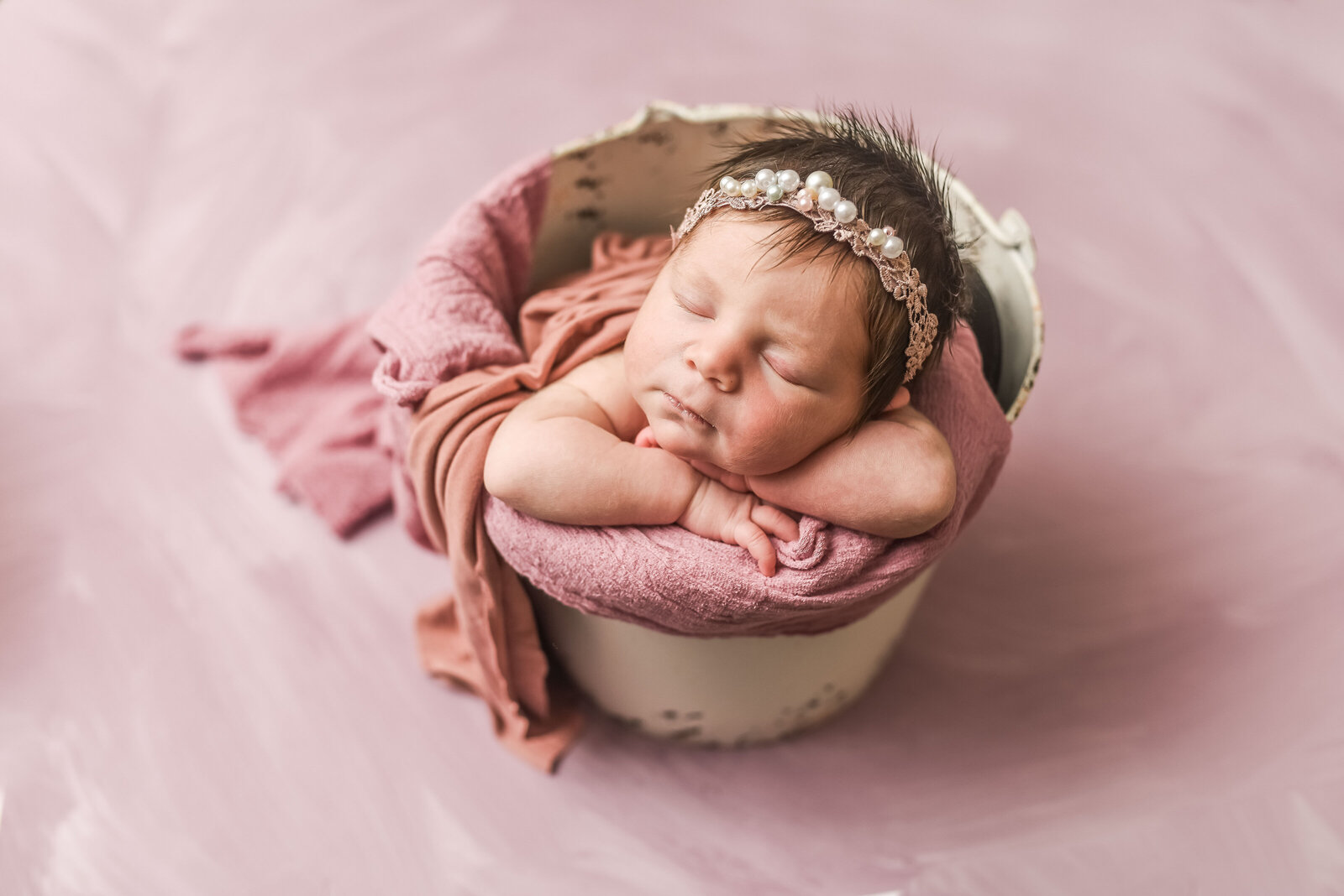 newborn girl wrapped in pink blanket sitting in basket with flowers  wearing a pink headband