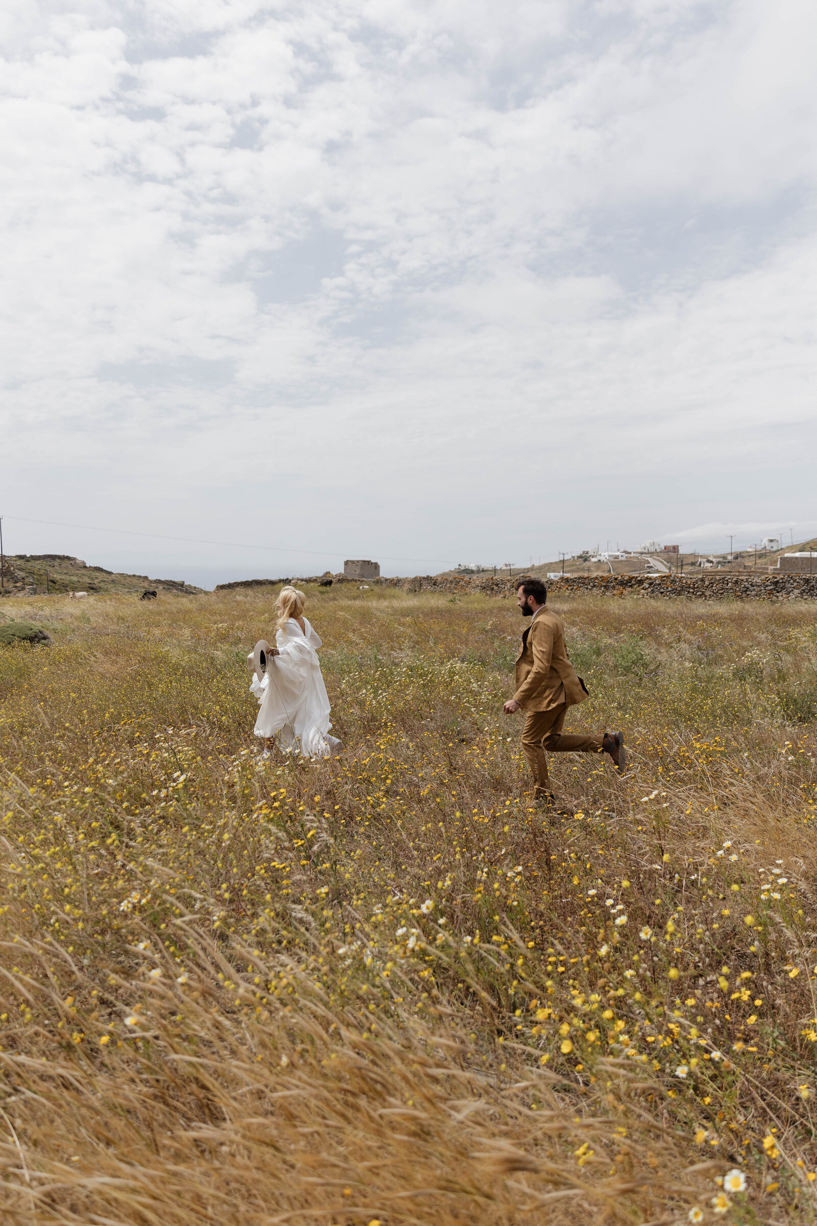 A newlywed couple running in a field with their elopement photographer.