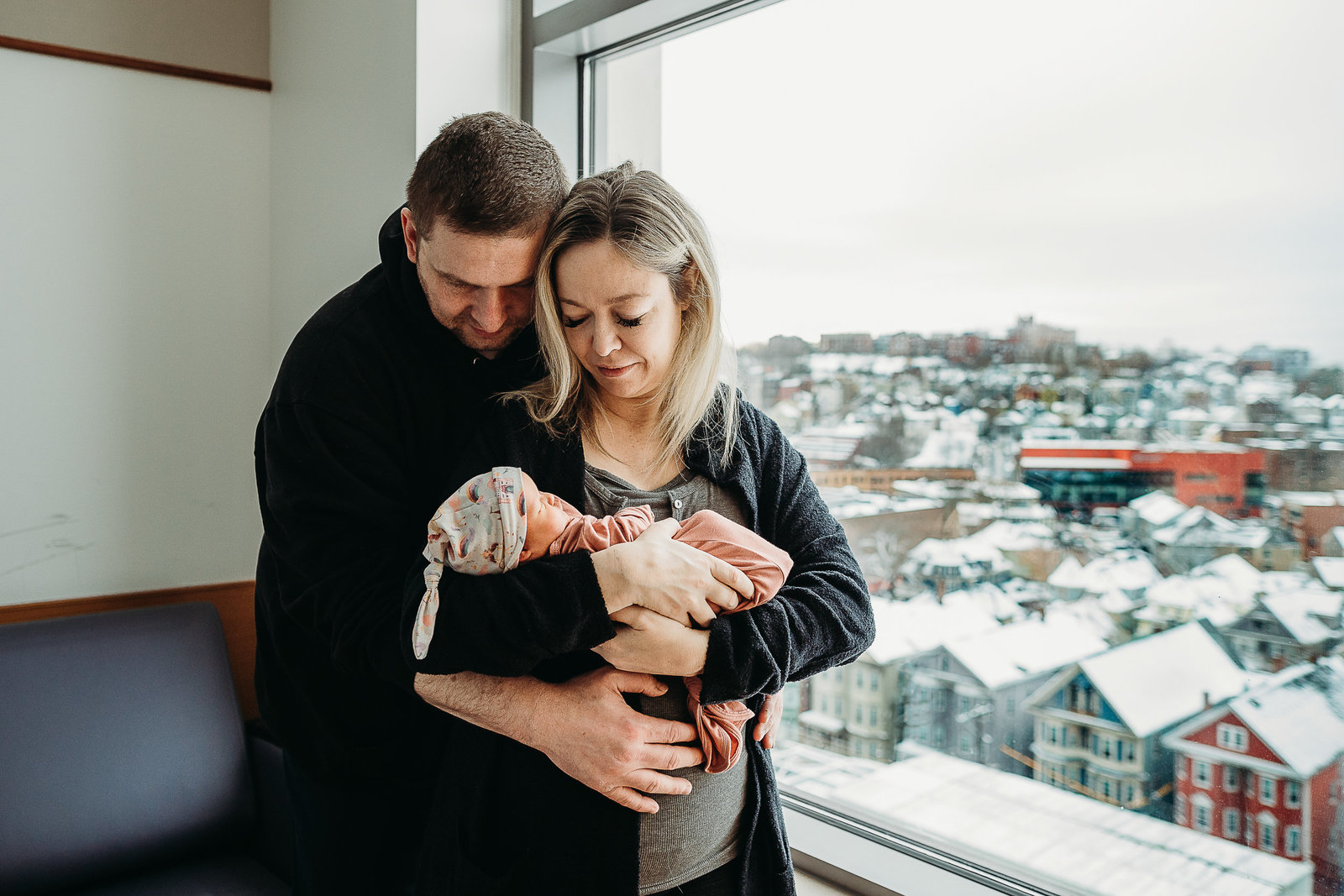 parents look down at new baby next to hospital window in winter