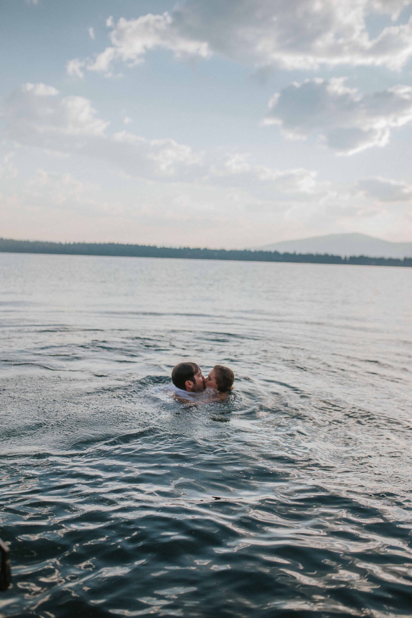 Sacramento Wedding Photographer captures bride and groom swimming in water kissing after beach wedding
