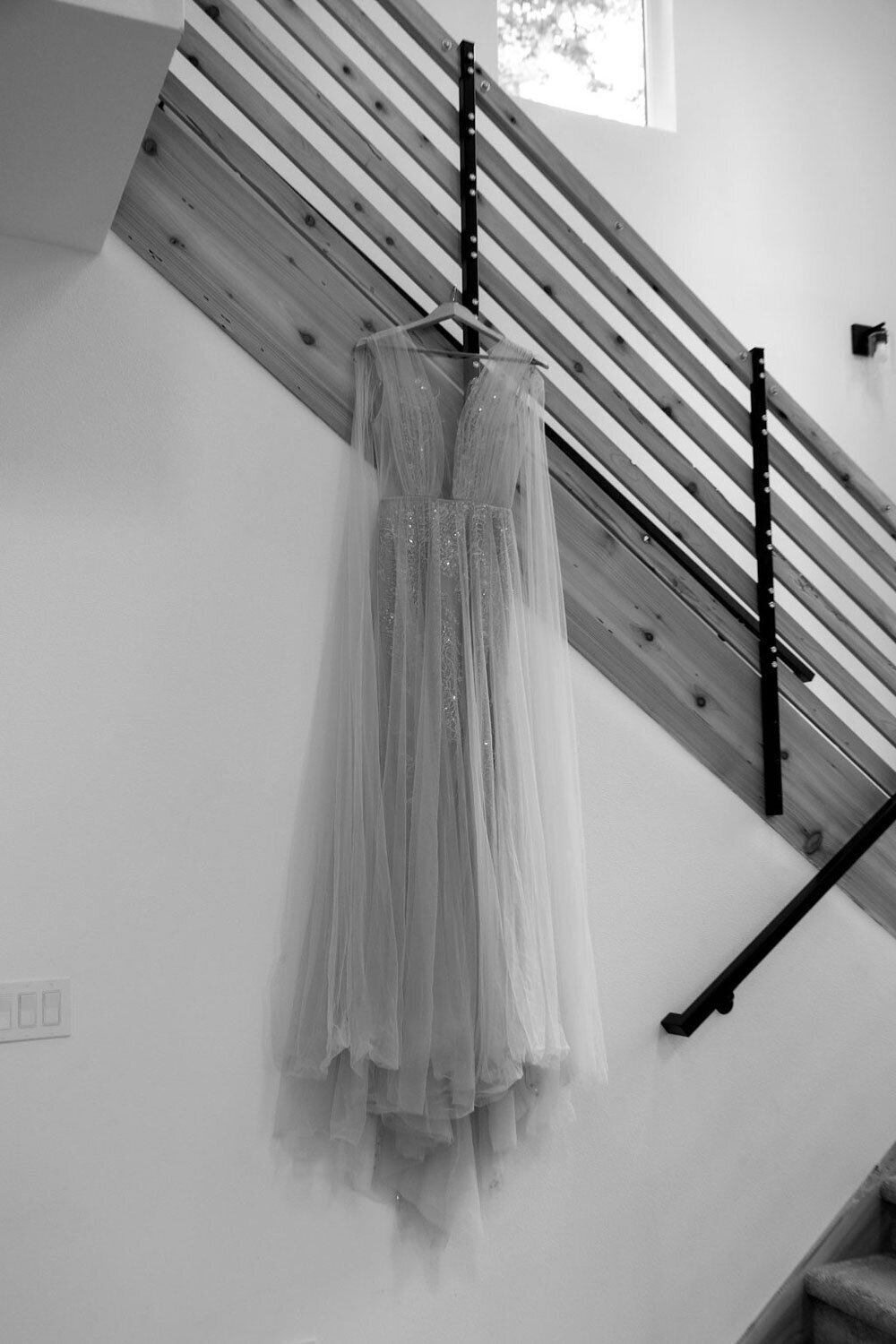 Flowing blush wedding gown hanging beside a wooden staircase
