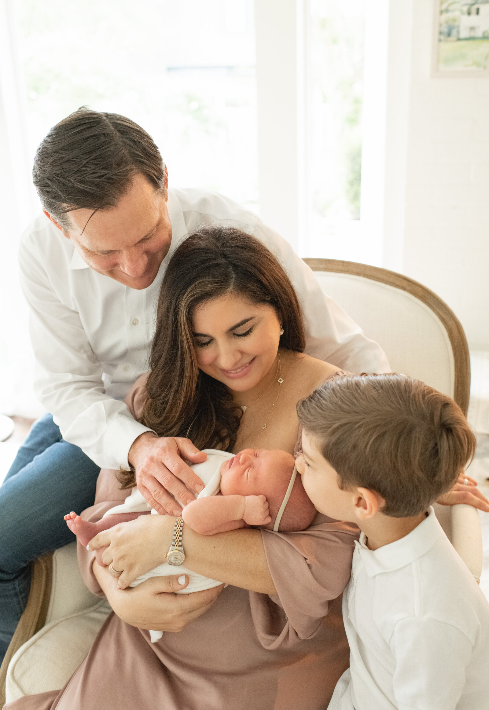 Family gathers around their newborn, sharing a loving moment. A heartfelt newborn session by Moments in Light Photography.