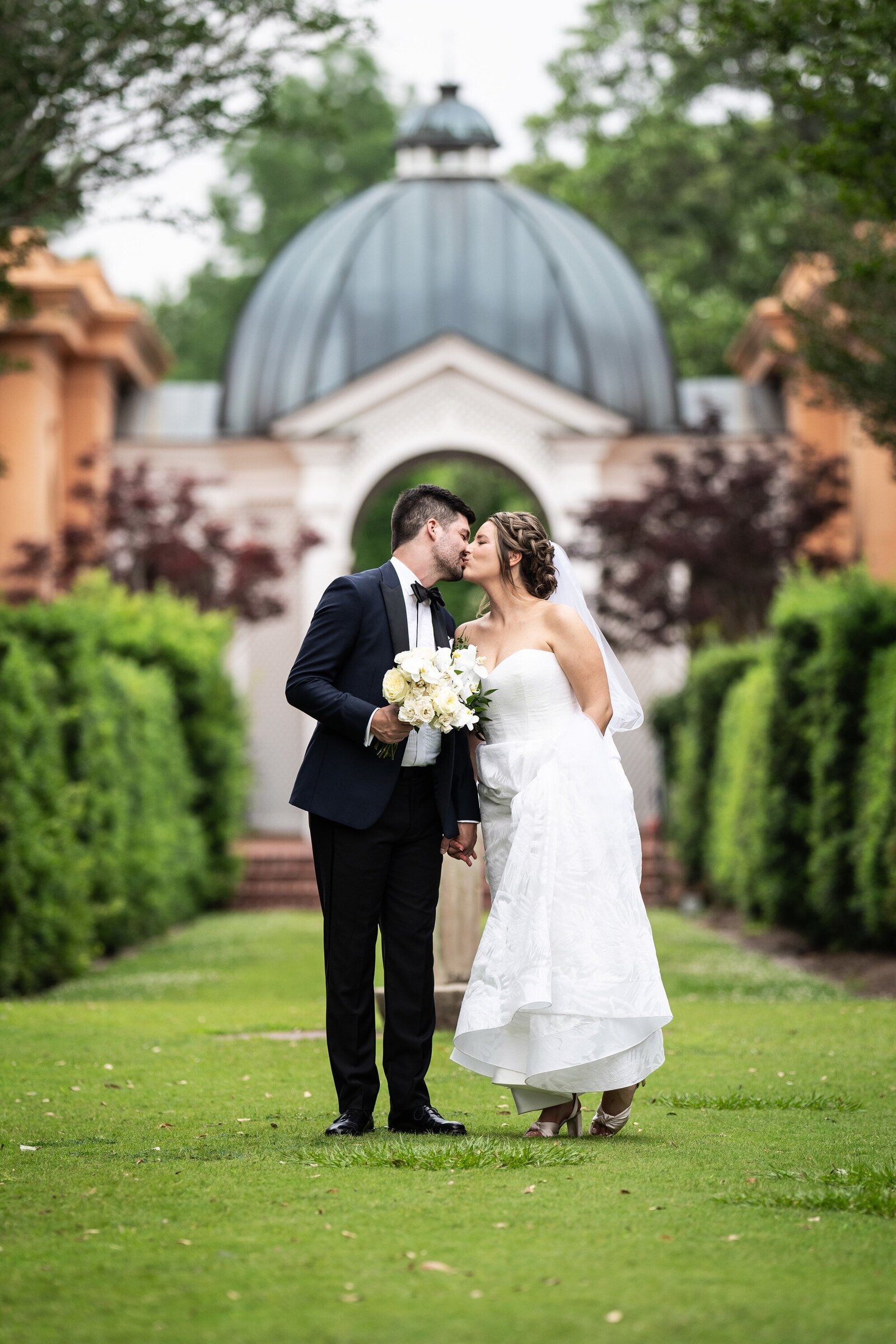 Bride and groom walking down grass with Pavilion of the Two Sisters in background