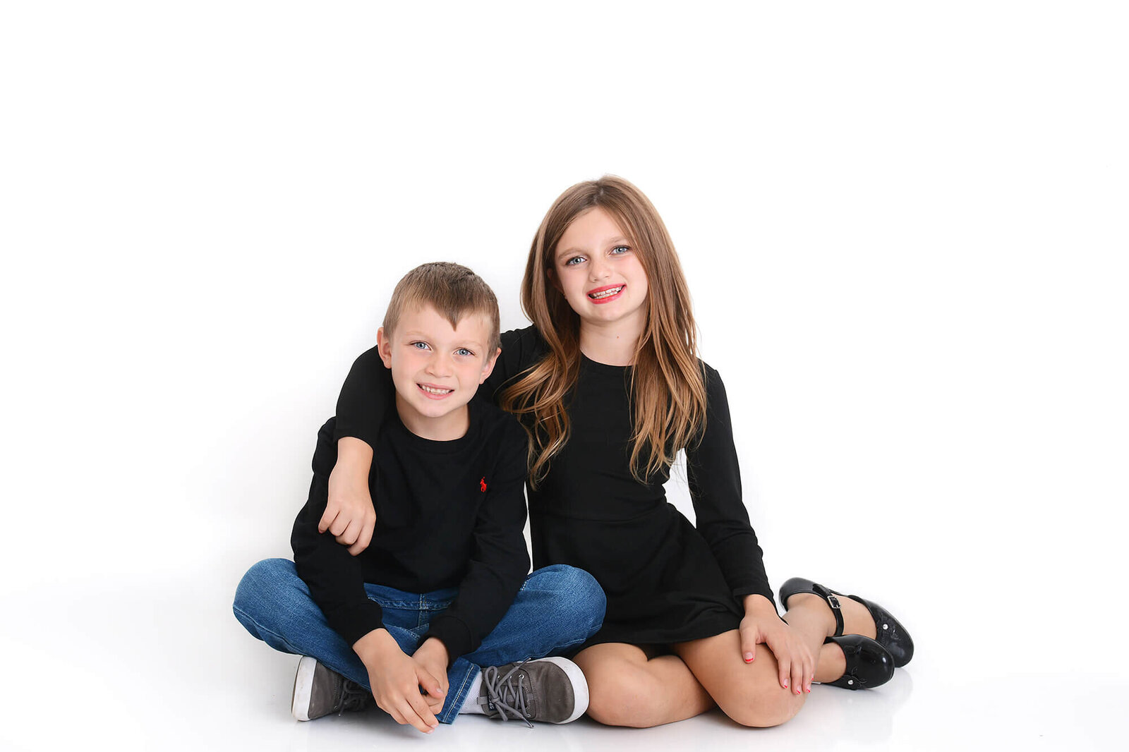 siblings cuddle up and smile at the camera at a photoshoot