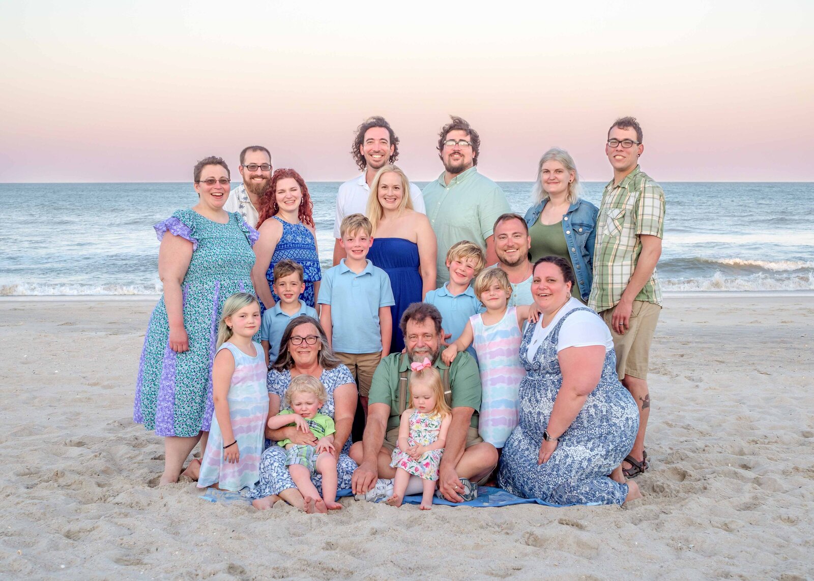 A multi-generational family poses on the sandy shores of Wrightsville Beach, dressed in coordinated blue and khaki outfits. The ocean waves and clear sky provide a beautiful backdrop, capturing the warmth and connection of family. Ideal for North Carolina family photography, highlighting beachside gatherings.