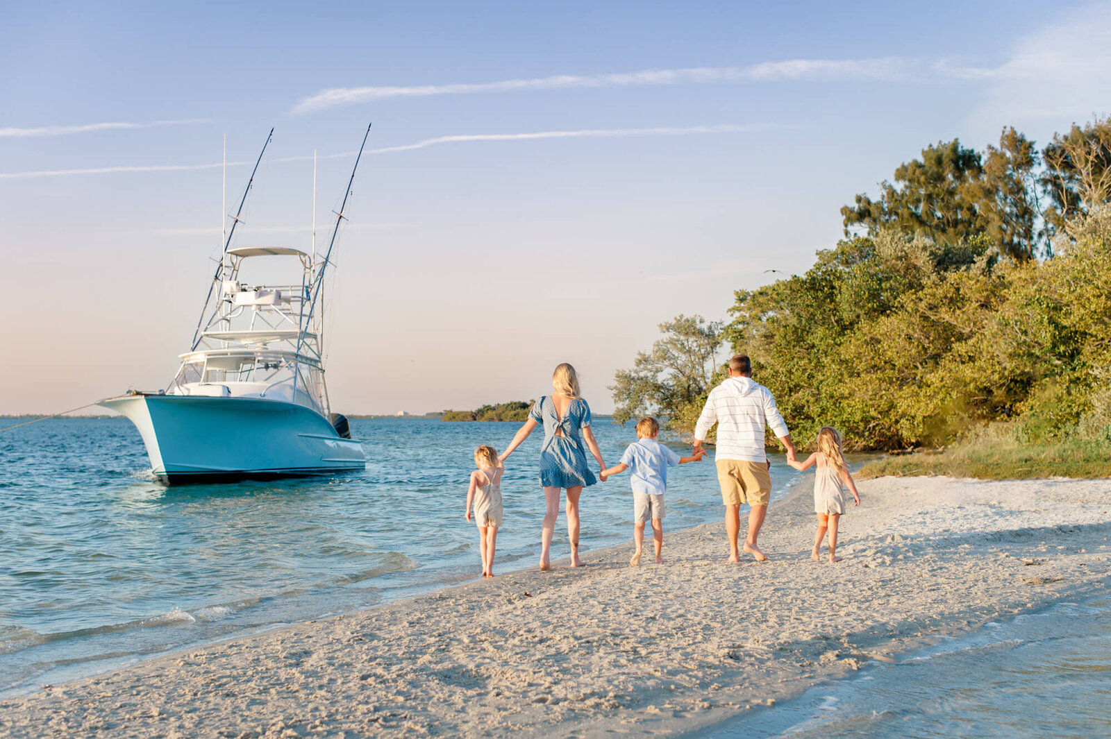 Family walking on an island toward their boat holding hands at sunset