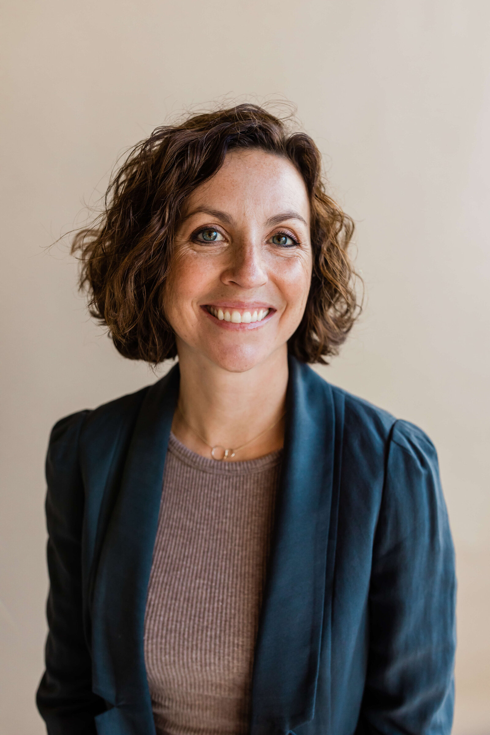 brunette with short hair smiling at the camera wearing blue cardigan