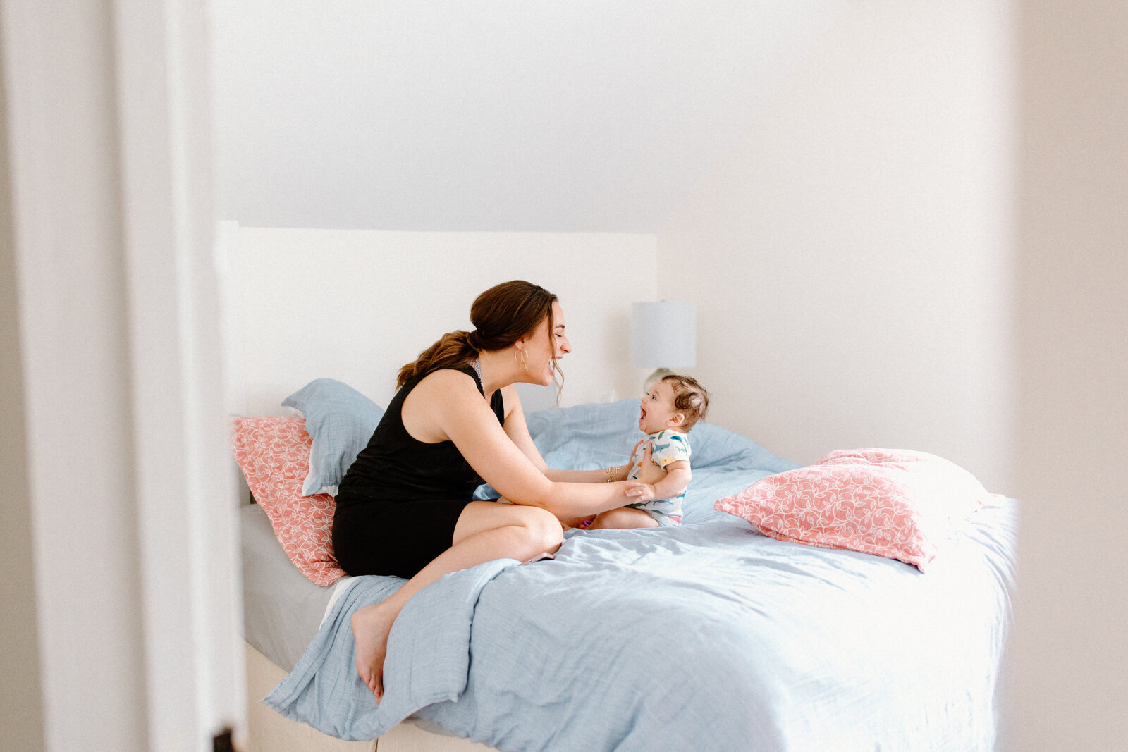 mother plays with baby in bright sunlit bedroom on the bed with a blue bedspread