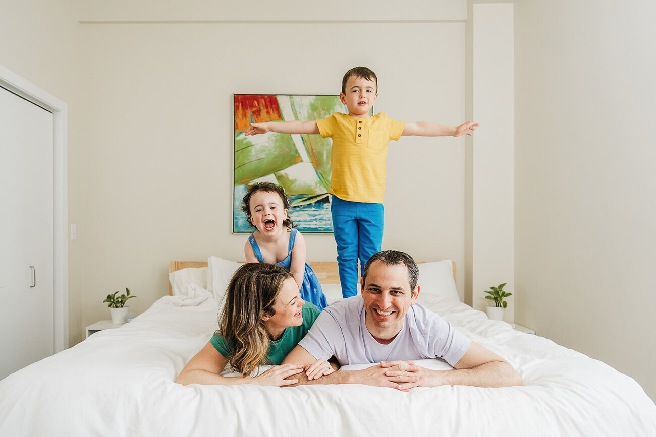 kids balance on parents backs while laying on bed