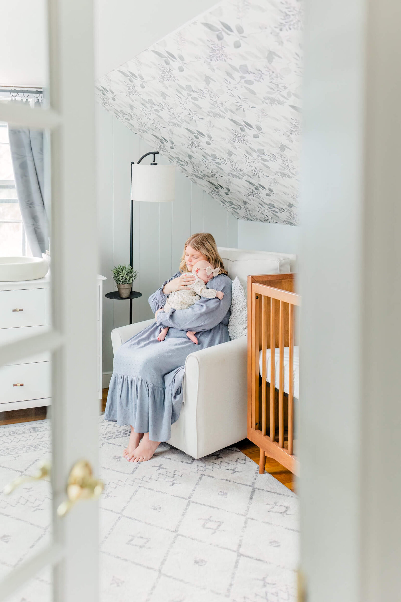 Mom sits in nursery chair, rocking baby to sleep