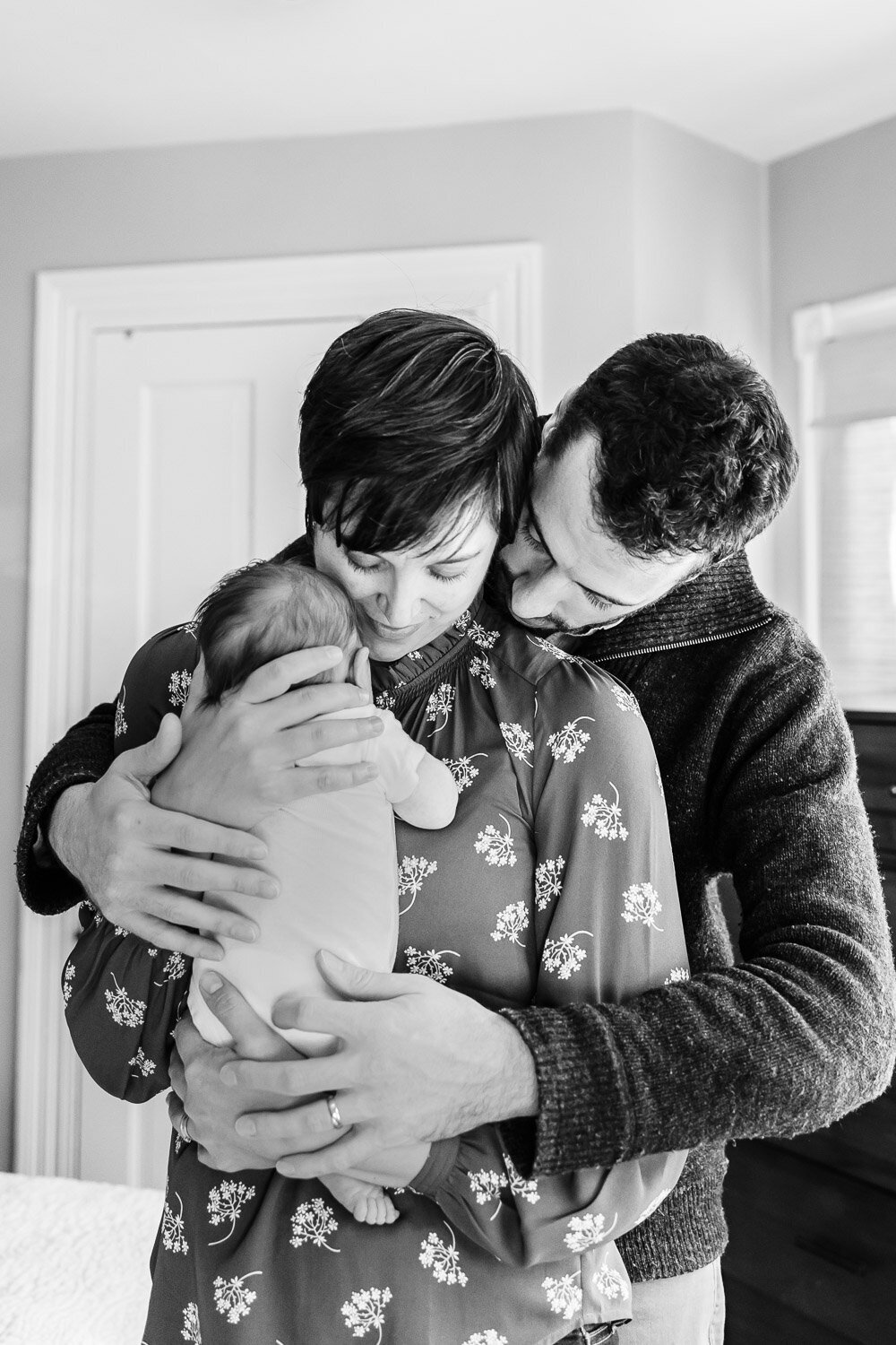 Black and white photo of couple embracing  newborn baby