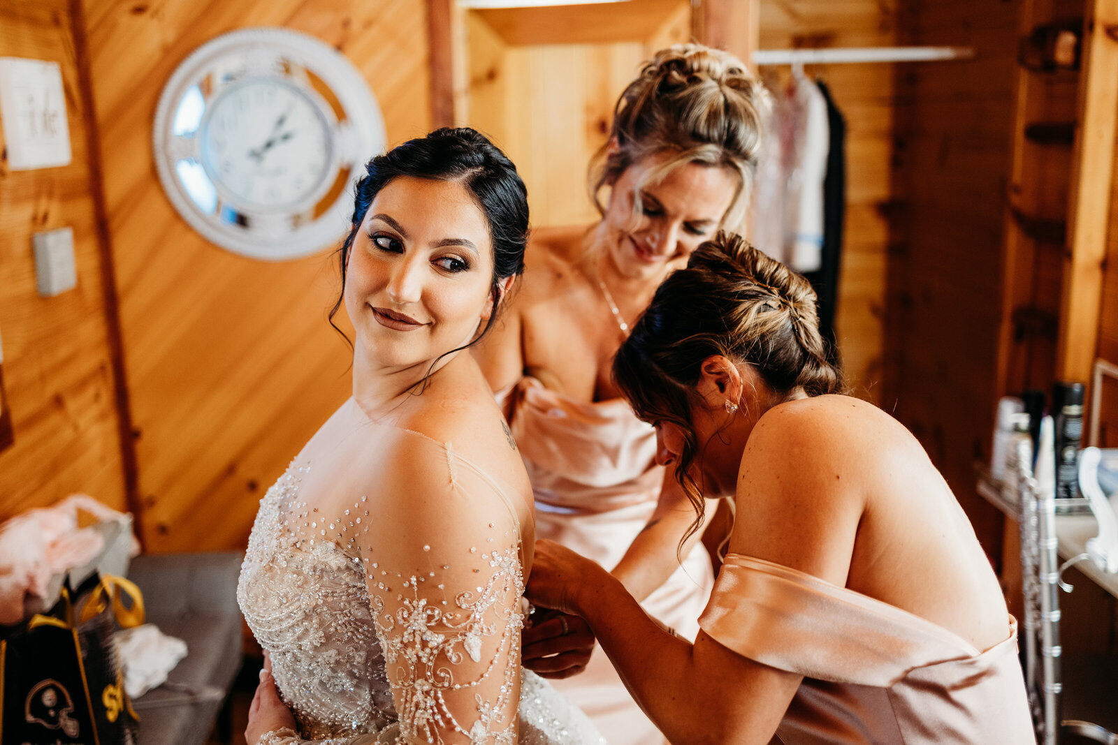 Bridesmaids help bride button up her wedding dress  in the  cabin before the ceremony