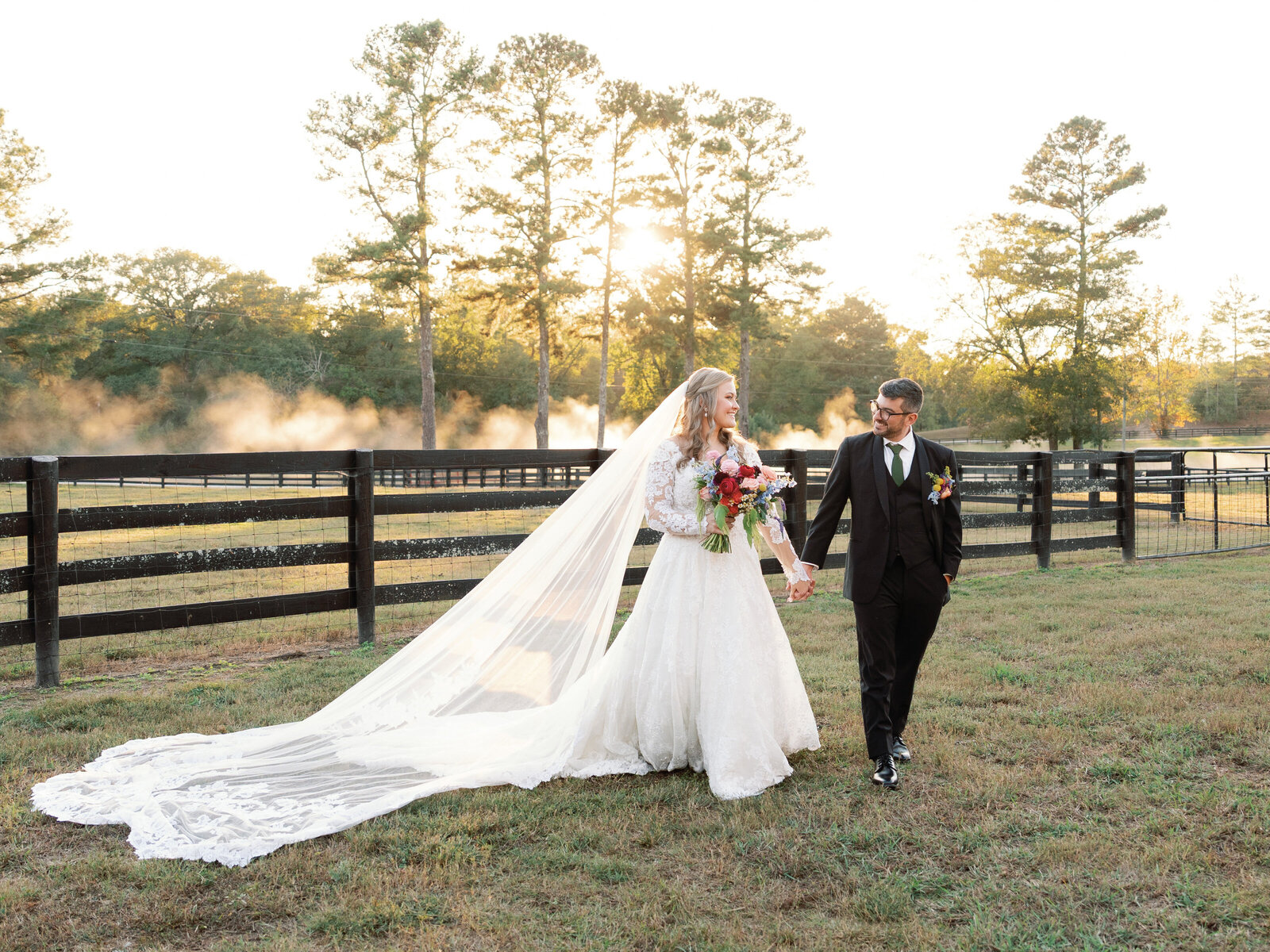 bride and groom at farm wedding walking with sunset in the background and black farm fence around