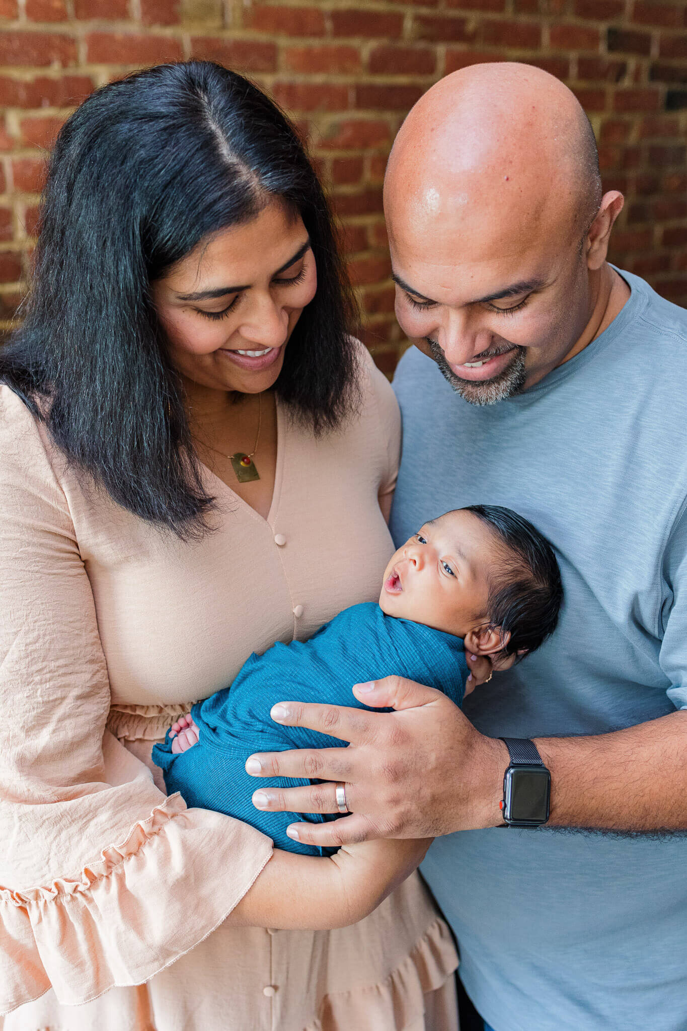 A couple holding their newborn son close and smiling down at him.