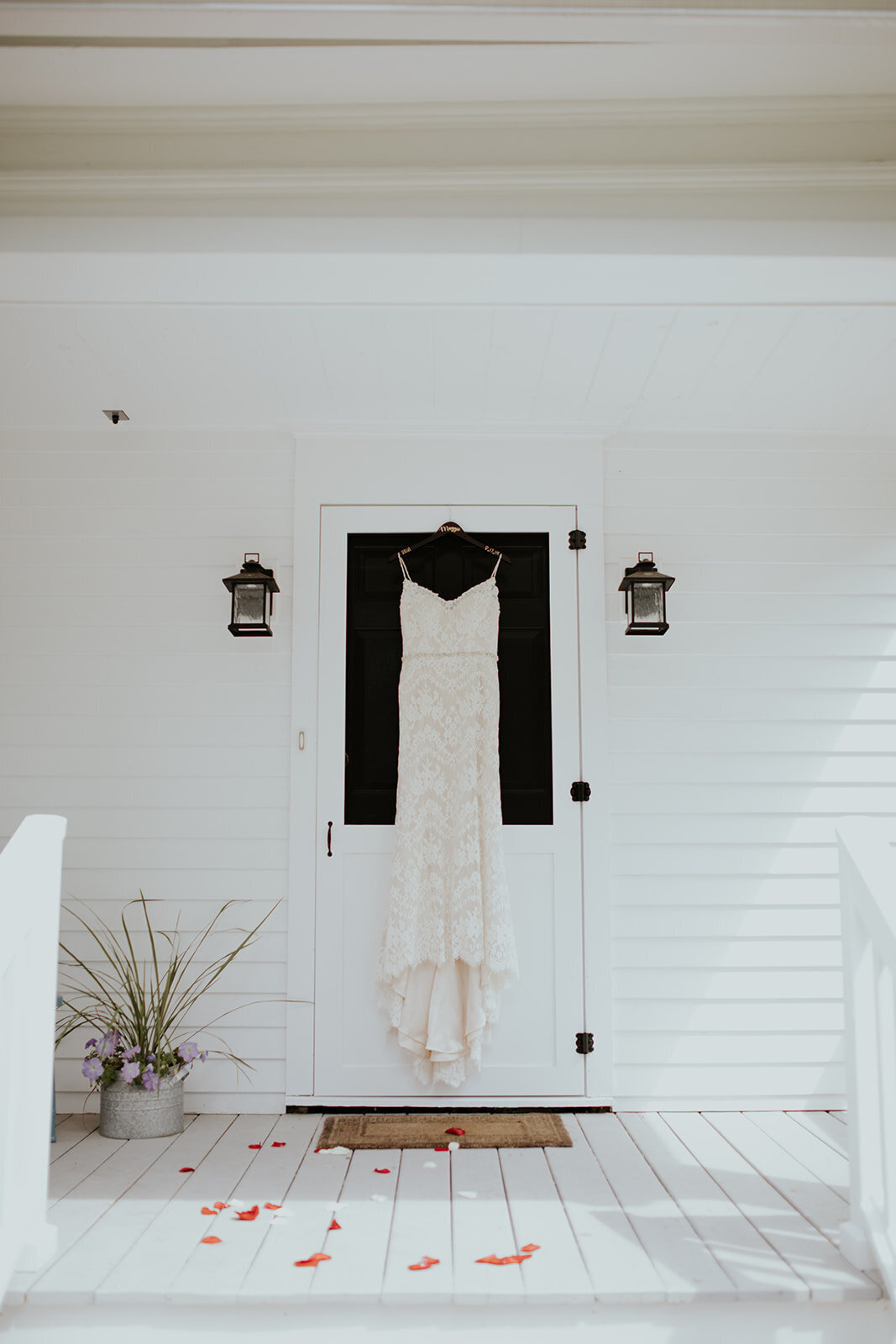 front door of white farmer cottage with a white bridal dress hanging from the  screen door