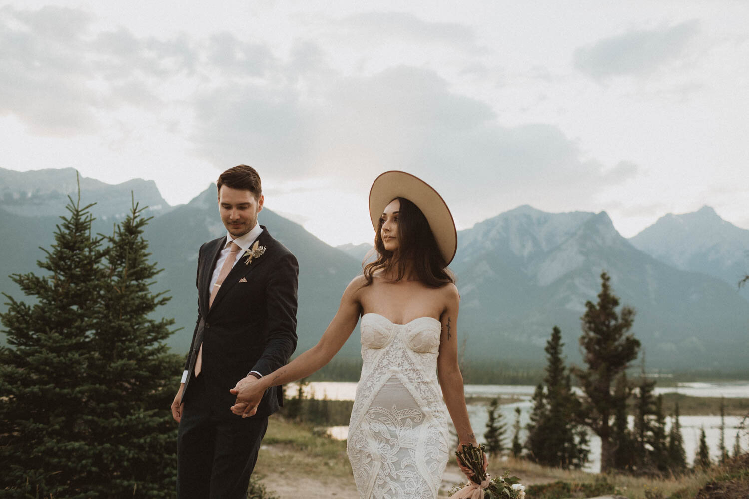 Bride in hat walking with the groom in a pine forest