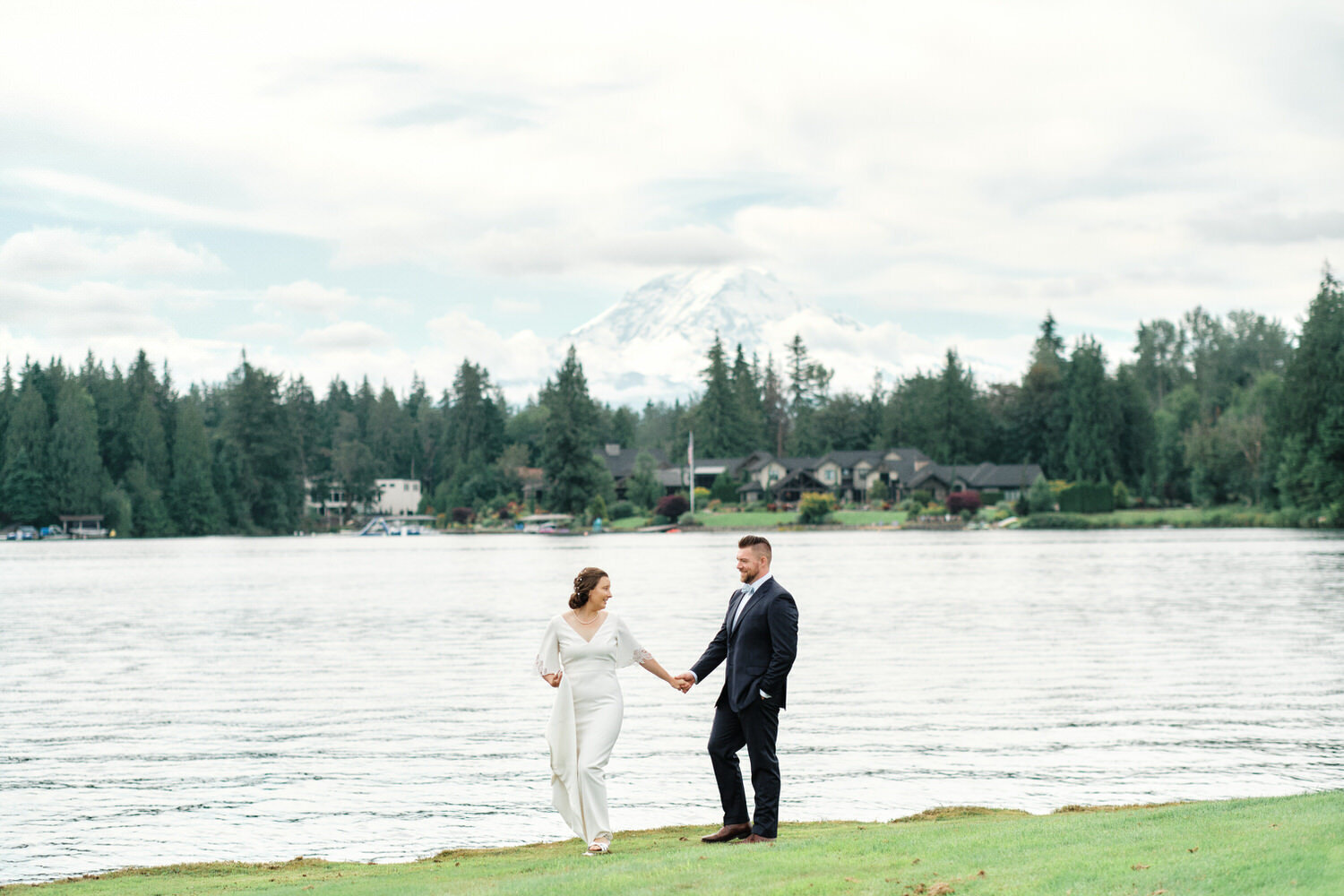 Bride and groom hold hands while walking along Lake Tapps