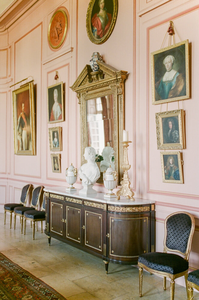 Light pink hallway with dark walnut sideboard, black formal chairs and formal portraits in gold frames