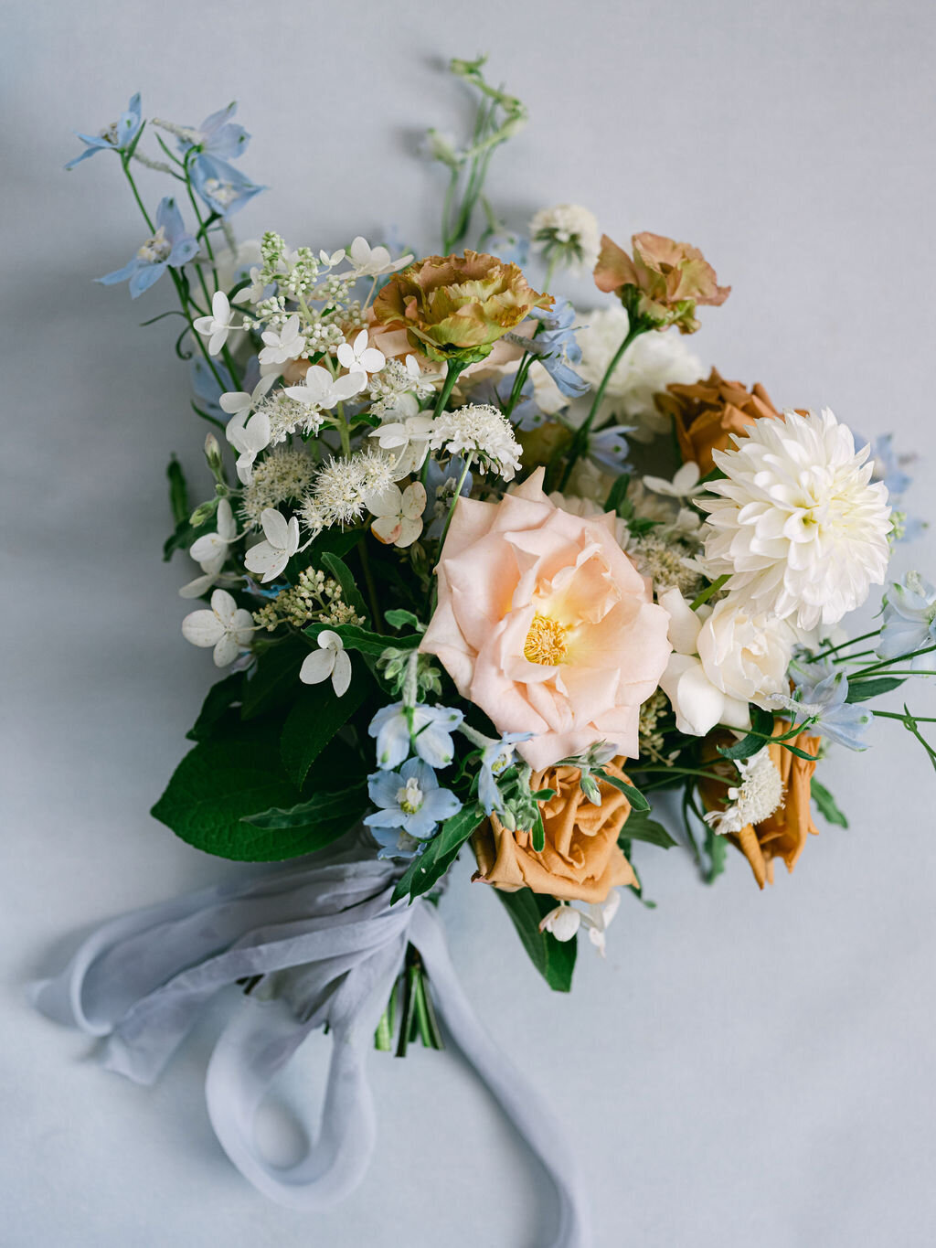 Bridal Bouquet with peach garden rose, white dahlia, toffee roses, white hydrangea, light blue delphinium and brown lisianthus and blue silk ribbon.