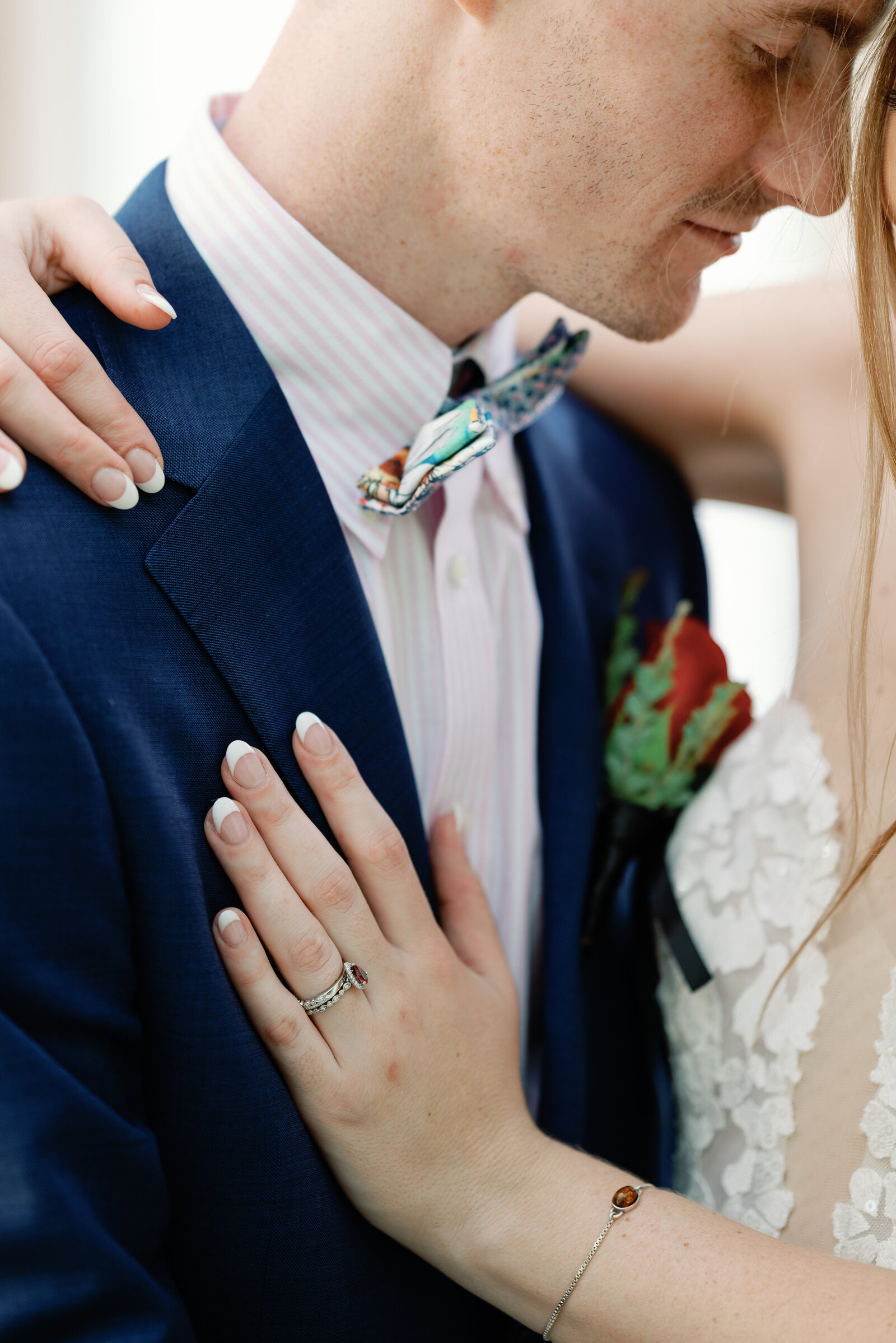 closeup of brides left hand, showing her rings, resting on grooms jacket lapel while he leans his head in toward hers