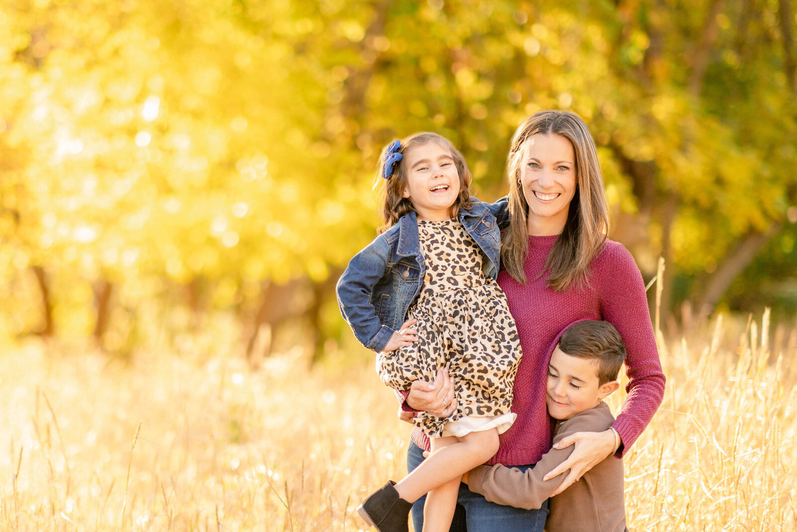 Mom holding her two young children in the woods with peak fall colors by Chicago family photographer Kristen Hazelton