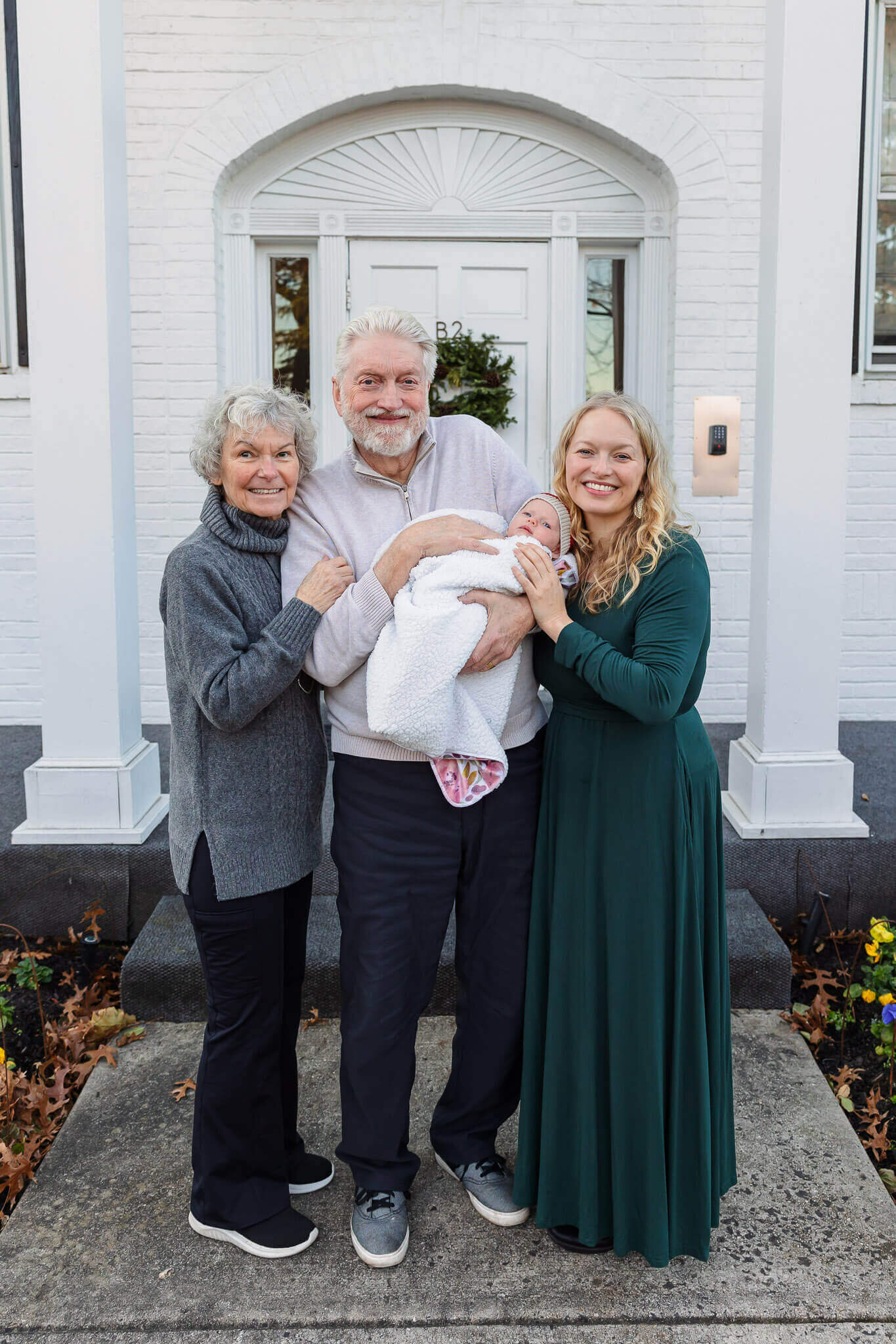 A mom with her newborn and her parents standing in front of a while building.