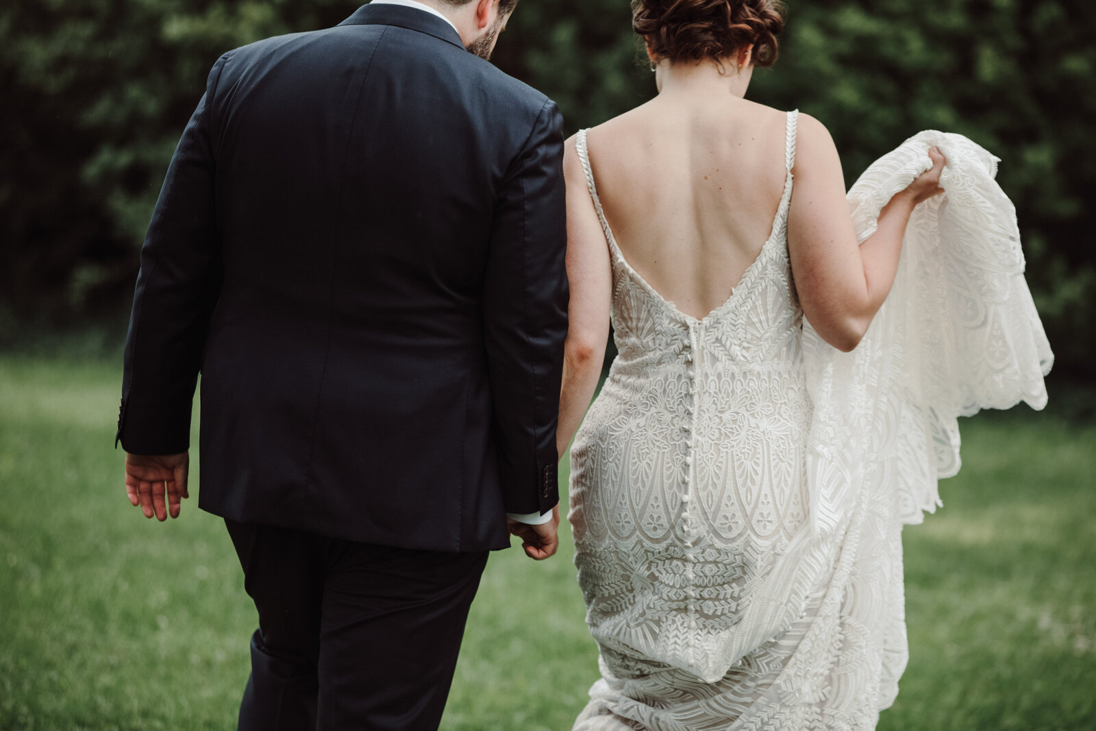 A bride and groom walk away holding her dress