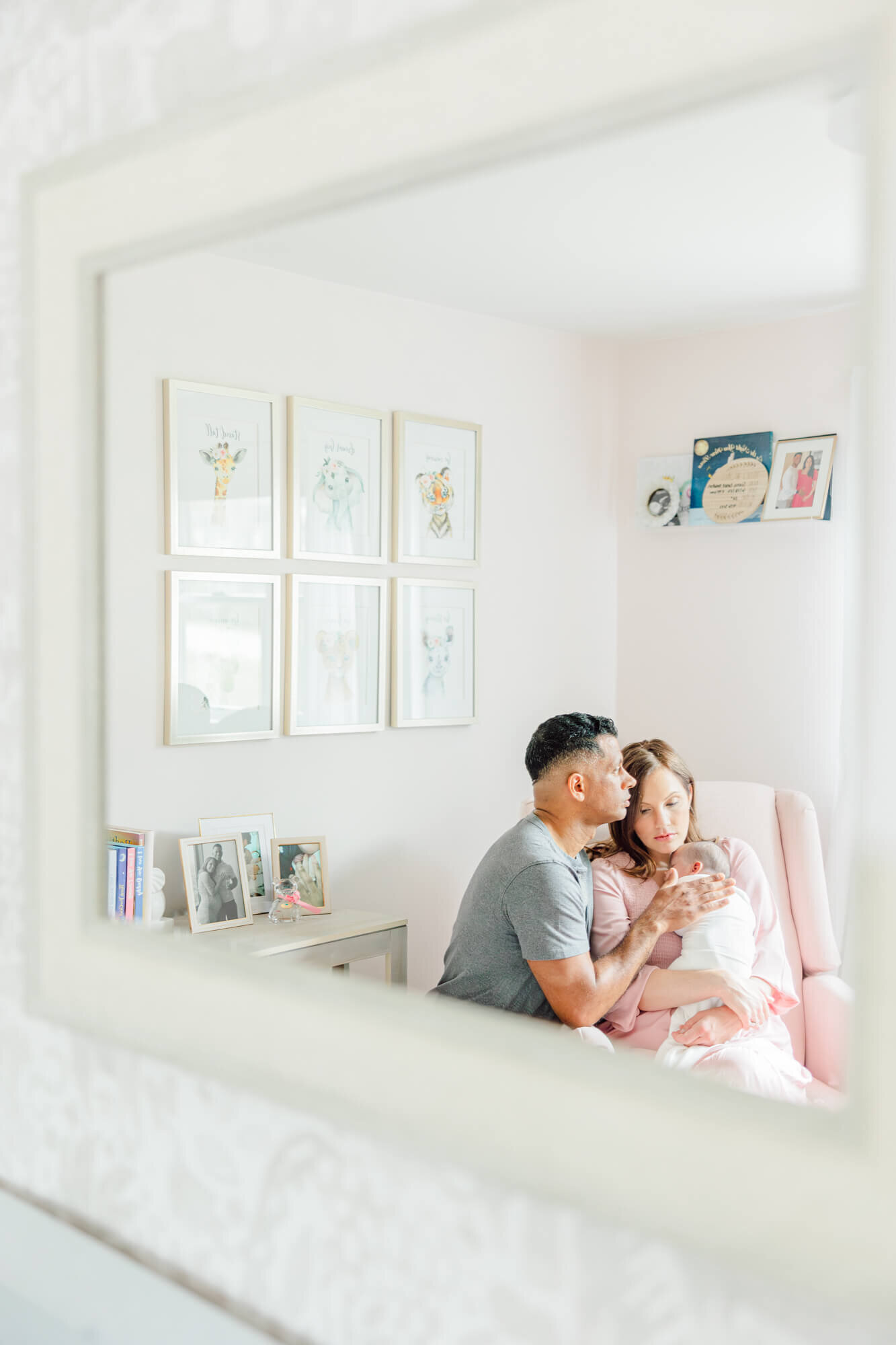 Mirror reflection of mom rocking her baby in the nursery with dad sitting next to her