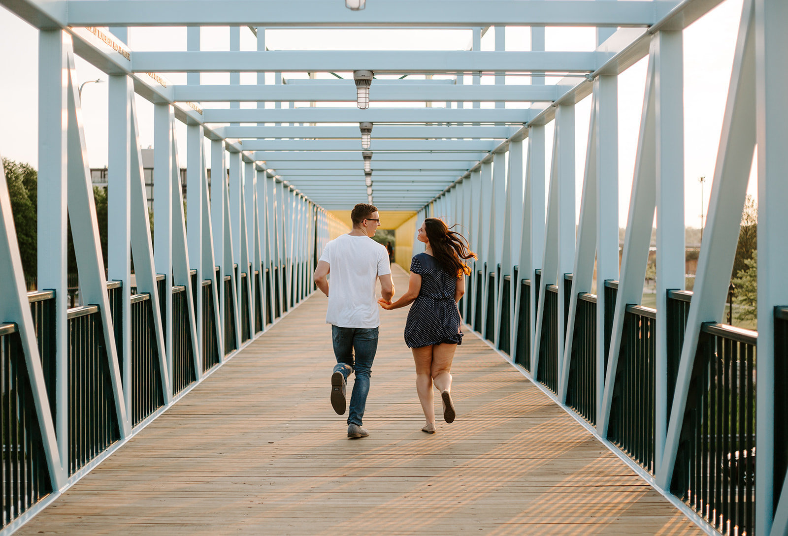 Couple running down a bridge holding hands during their engagement session
