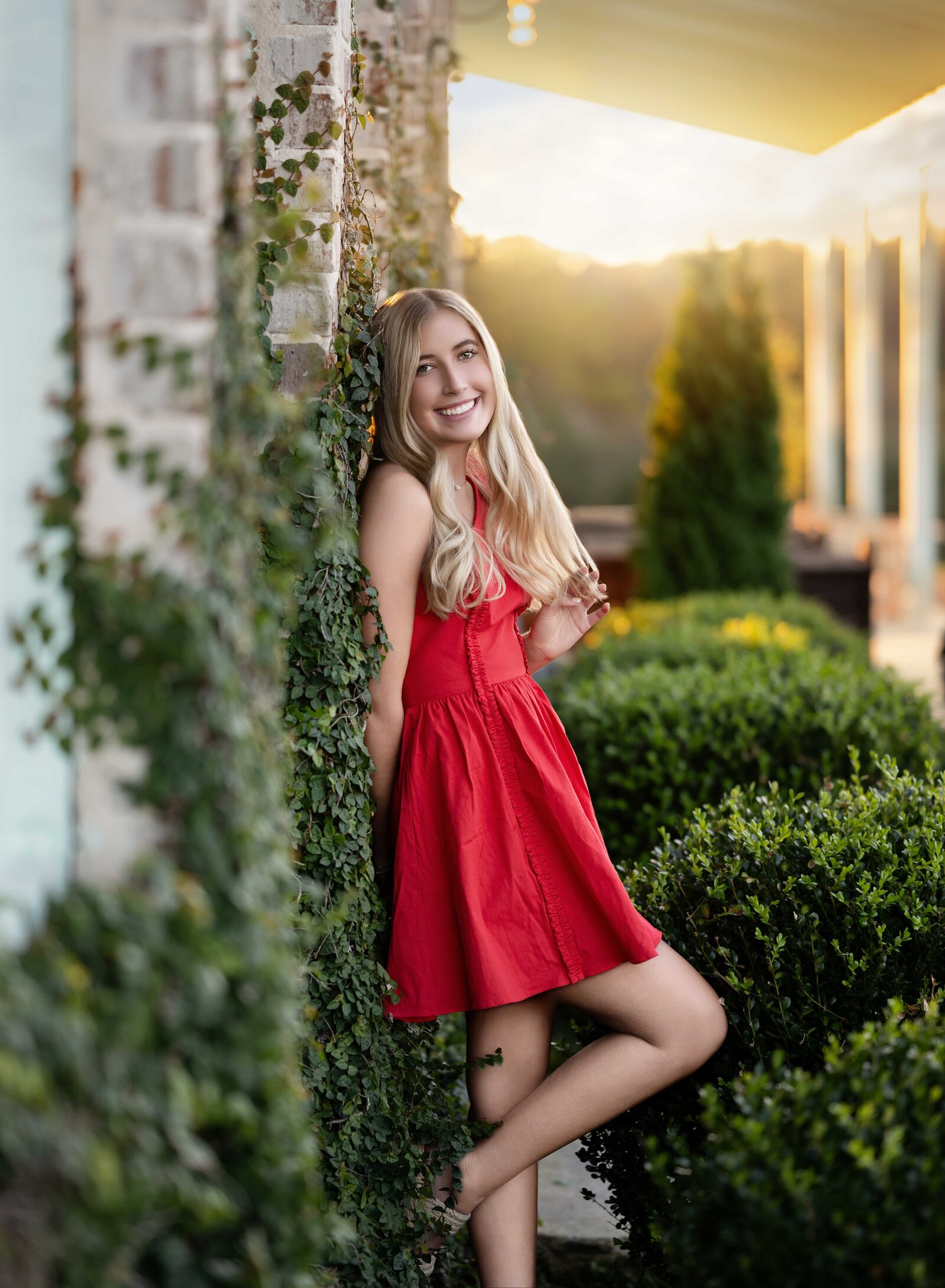 Girl in red dress leaning on ivy wall taking Senior photos.Senior graduation photos taken by Jenni Nikki Photography in Atlanta, GA