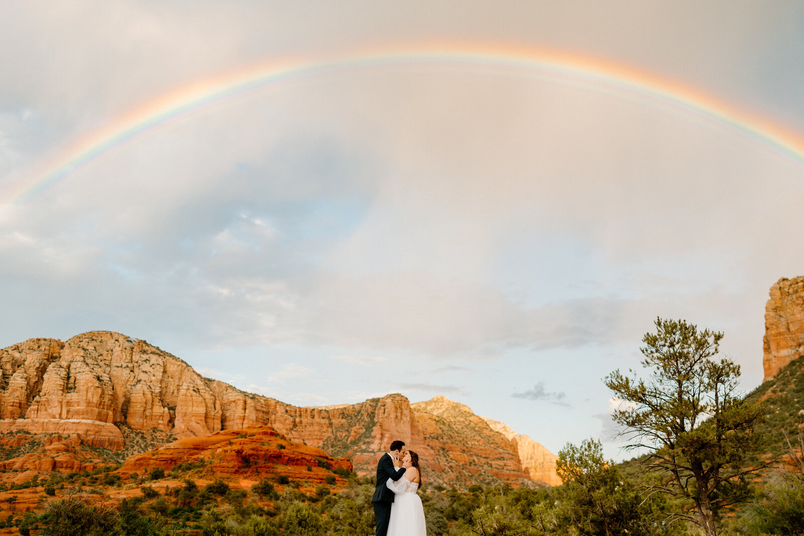 newlyweds kiss under rainbow in arizona landscape