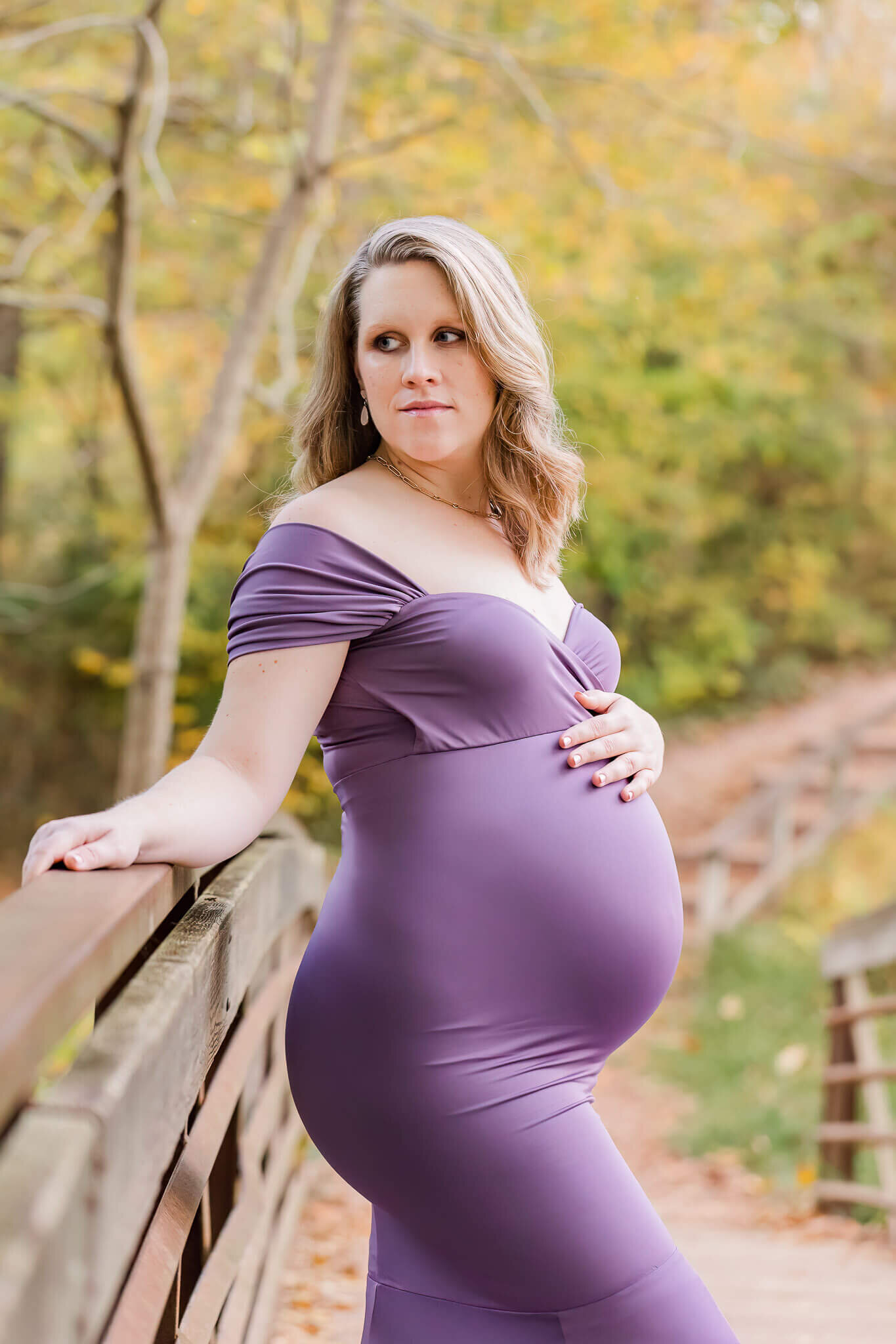 A beautiful pregnant woman in purple leaning against a bridge for her maternity portrait session.