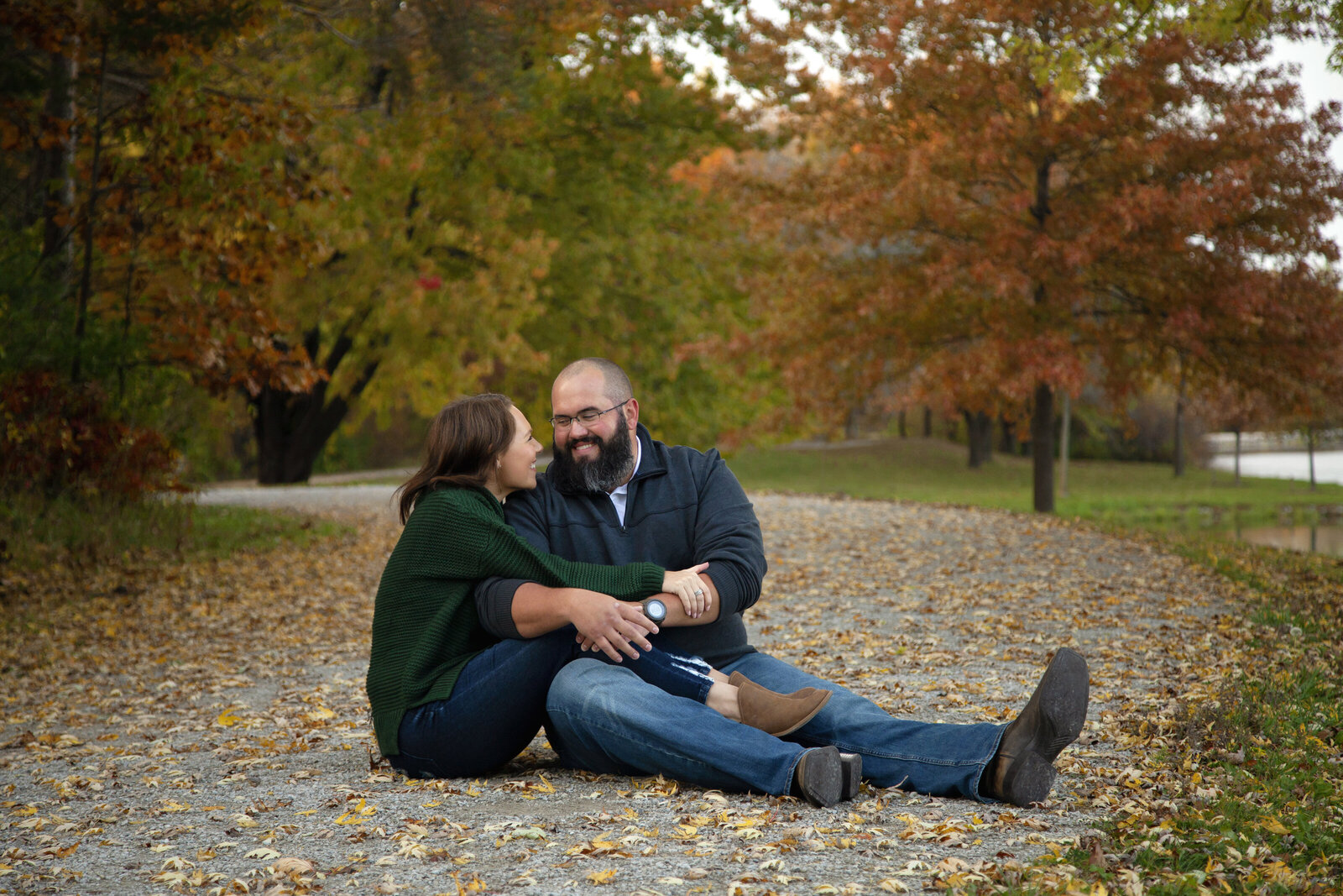 Couple sitting on leaf covered path, intertwined,smiling at each other.