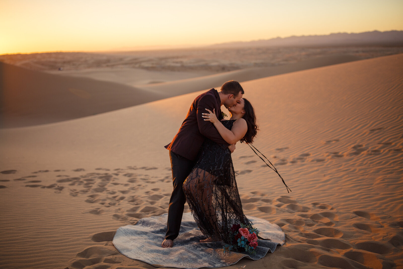 bride with black wedding dress kissing groom in the sand dunes