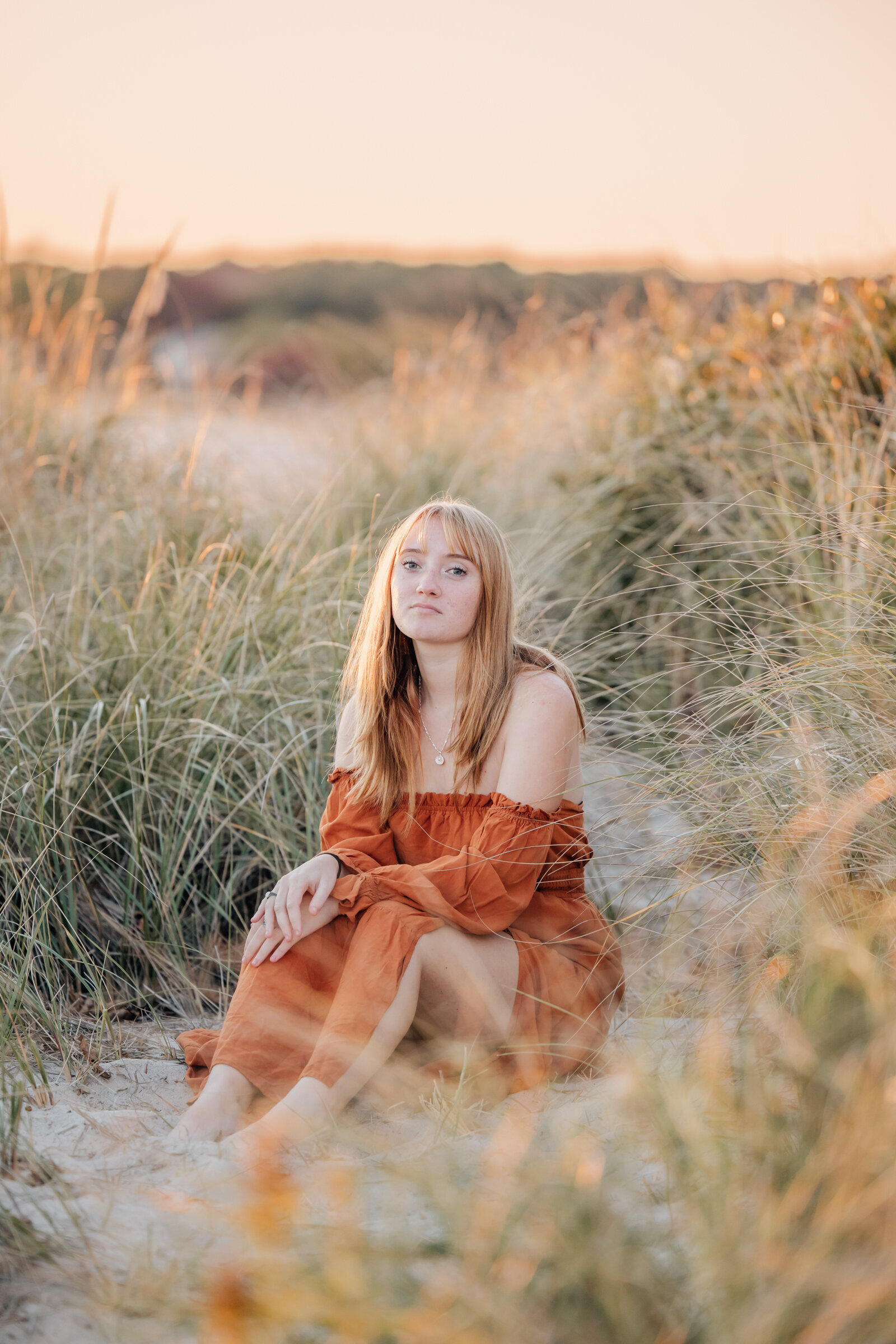 high school senior girl in orange dress with blond hair in tall beach grass