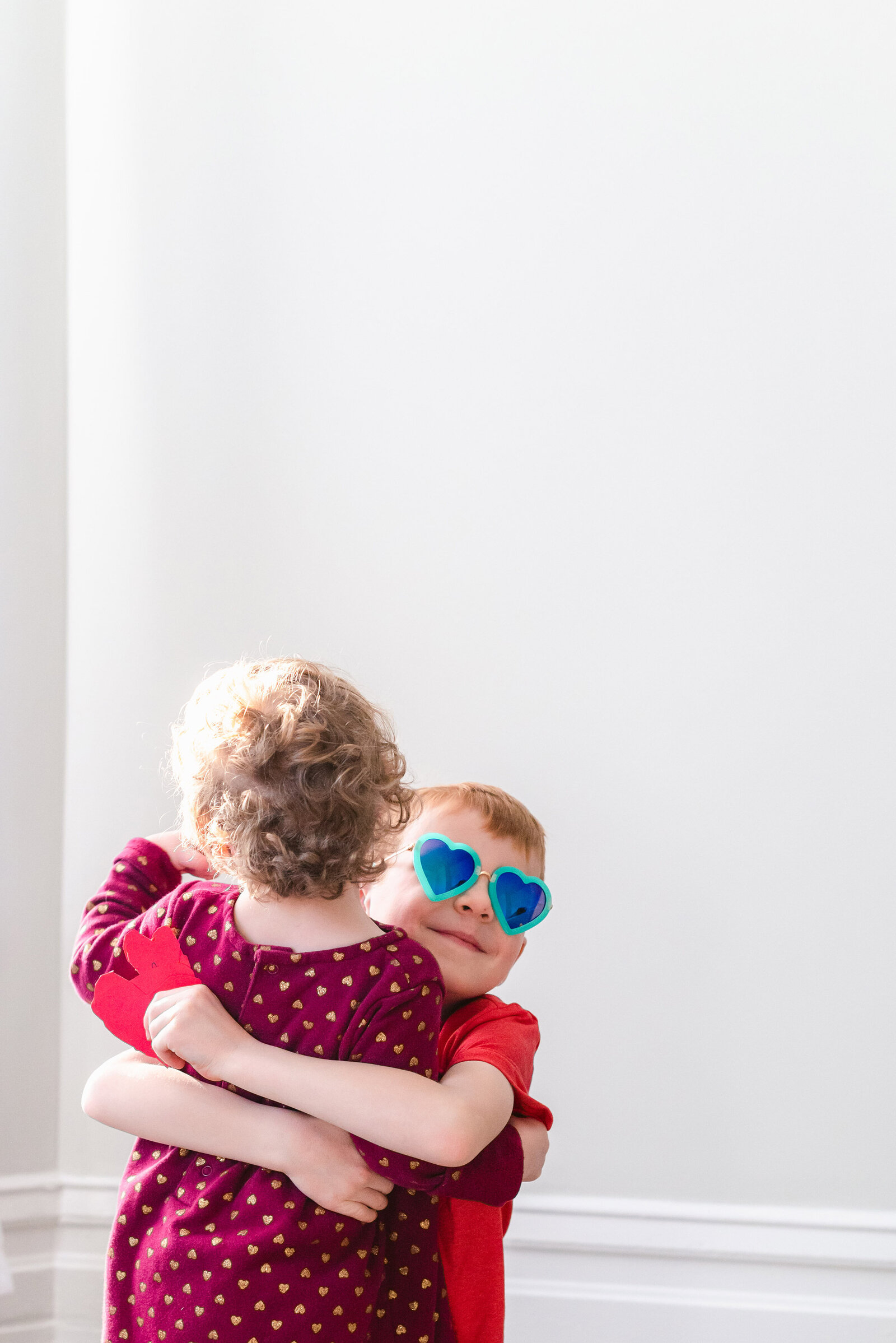 Brother wearing heart sunglasses hugging his toddler sister for valentine's day photo mini sessions