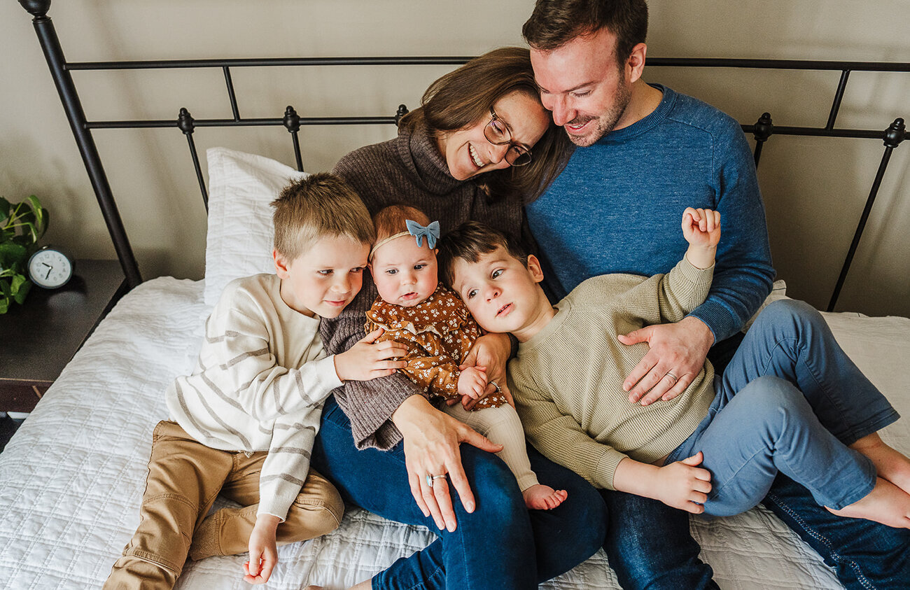 family of five snuggles on bed during in home boston family photo shoot