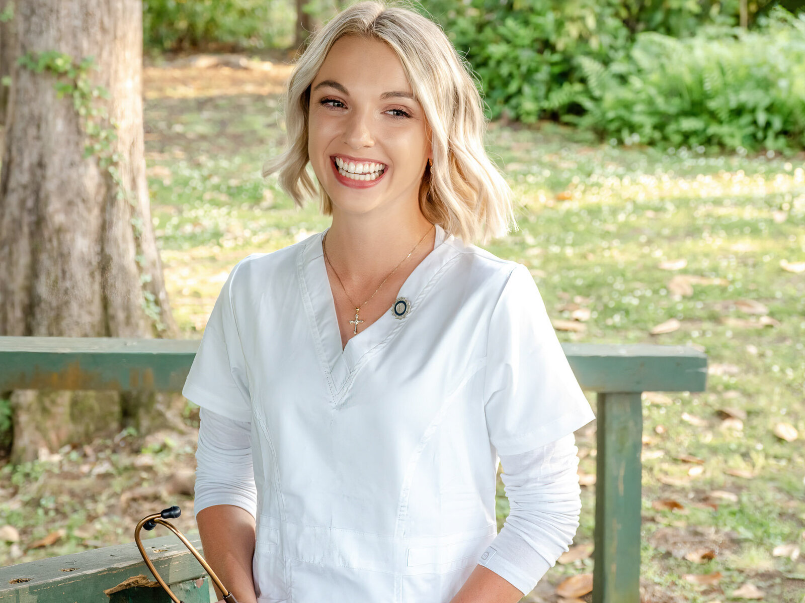 A UNCW senior in white nursing scrubs smiling brightly, standing in a lush outdoor setting in Wilmington, North Carolina. This image reflects career aspirations, ideal for those looking for personalized and meaningful senior photography.