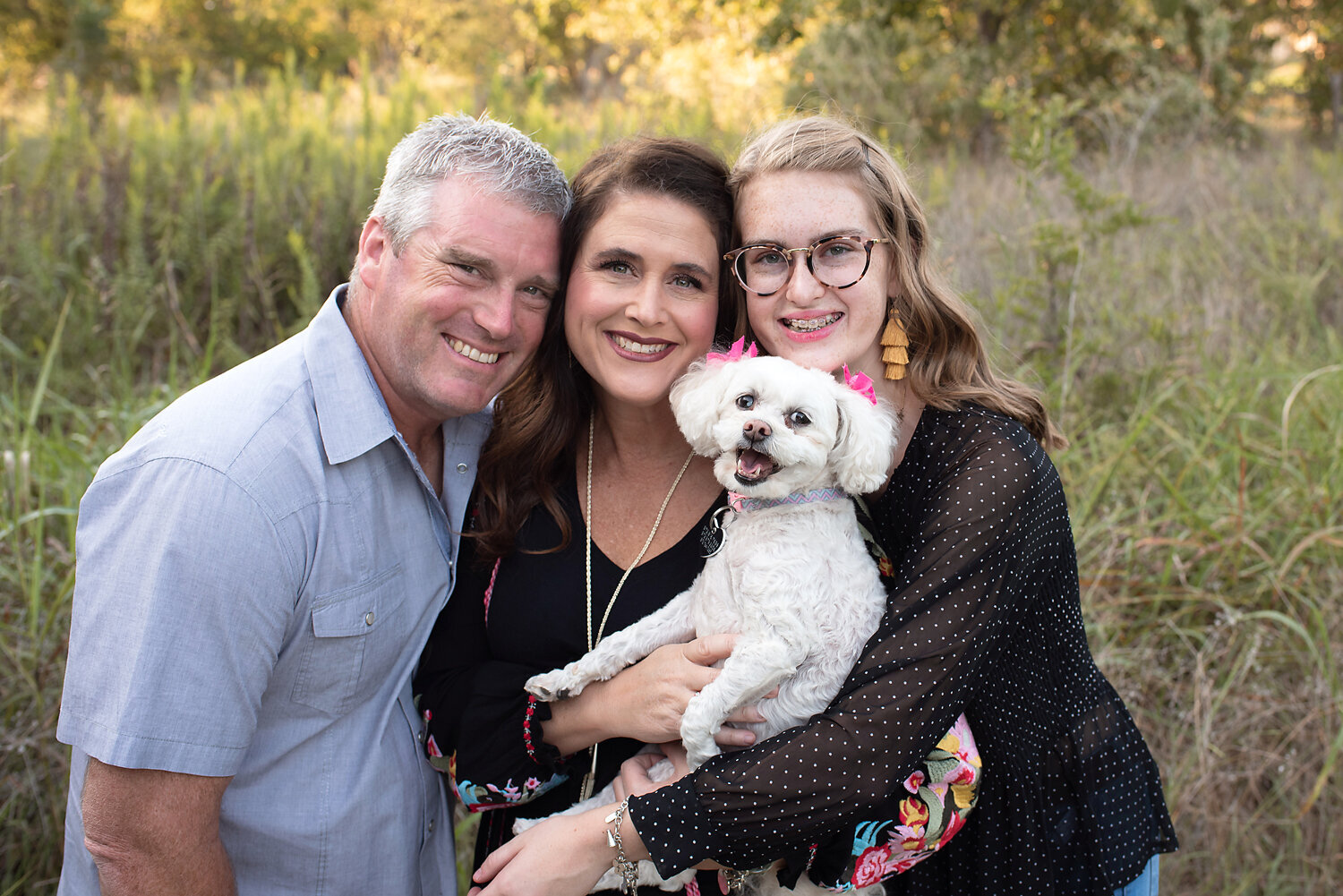 A family smiling and cuddling their small white dog.