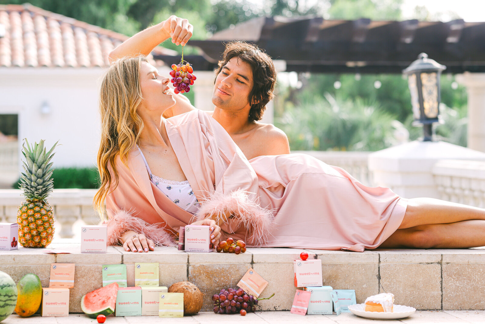 Model feeding grapes on bed grecian inspired lifestyle product photoshoot san diego commercial photographer