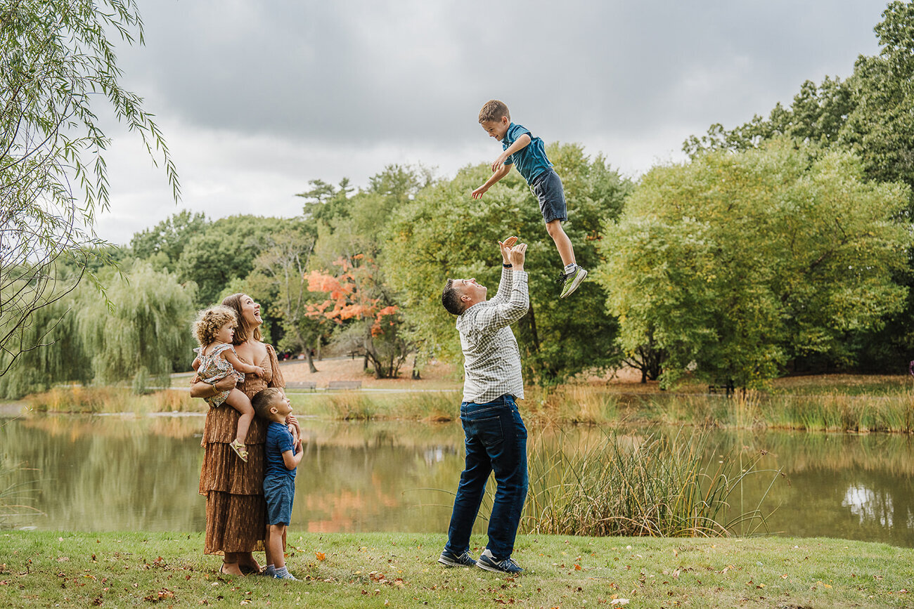 dad tosses son in air while mother looks on in front of lake